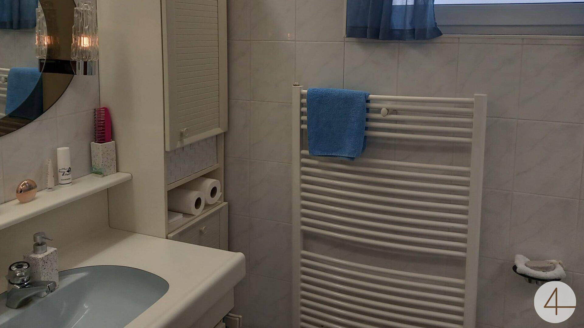 Helles Badezimmer mit Waschbecken, Spiegelschrank, beheiztem Handtuchhalter und kleinem Fenster.