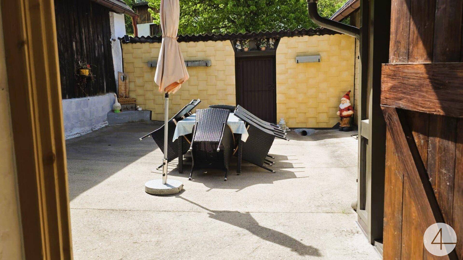 Sonniger Außenbereich mit Gartenmöbeln, Sonnenschirm und einer gelben Wandverkleidung.