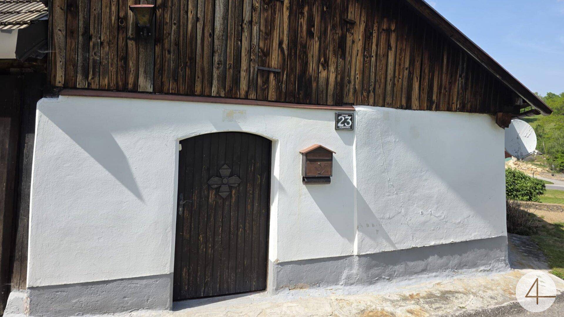 Alte Hausfassade mit Holztür, weißem Putz und verwitterter Holzverkleidung im oberen Bereich.