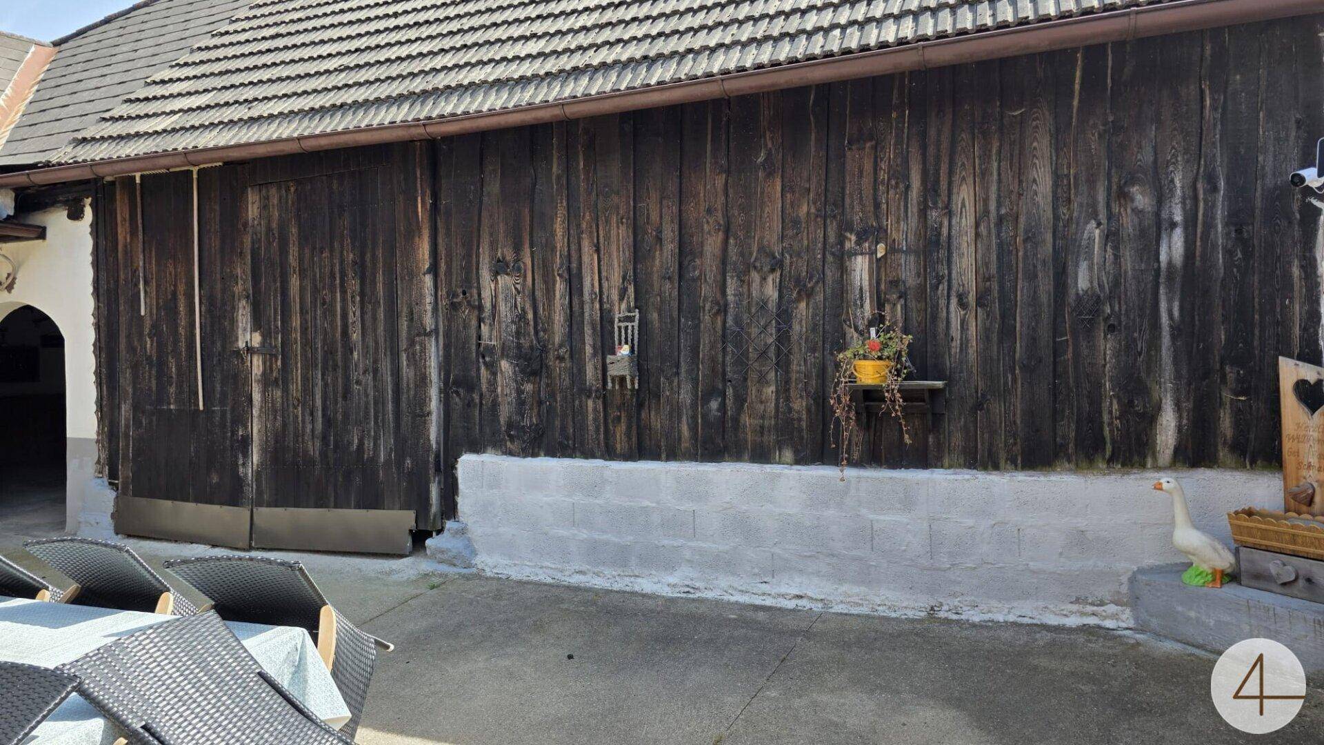 Dunkle Holzfassade eines Gebäudes mit einem Betonsockel und einem Teil des Außenbereichs.