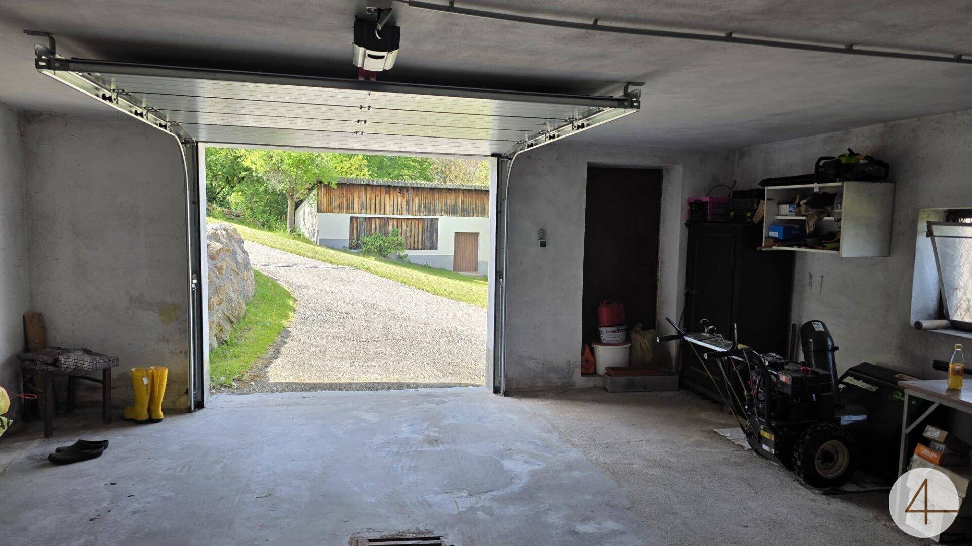Geräumige Garage mit offenem Tor, Betonboden und Blick auf die Einfahrt.