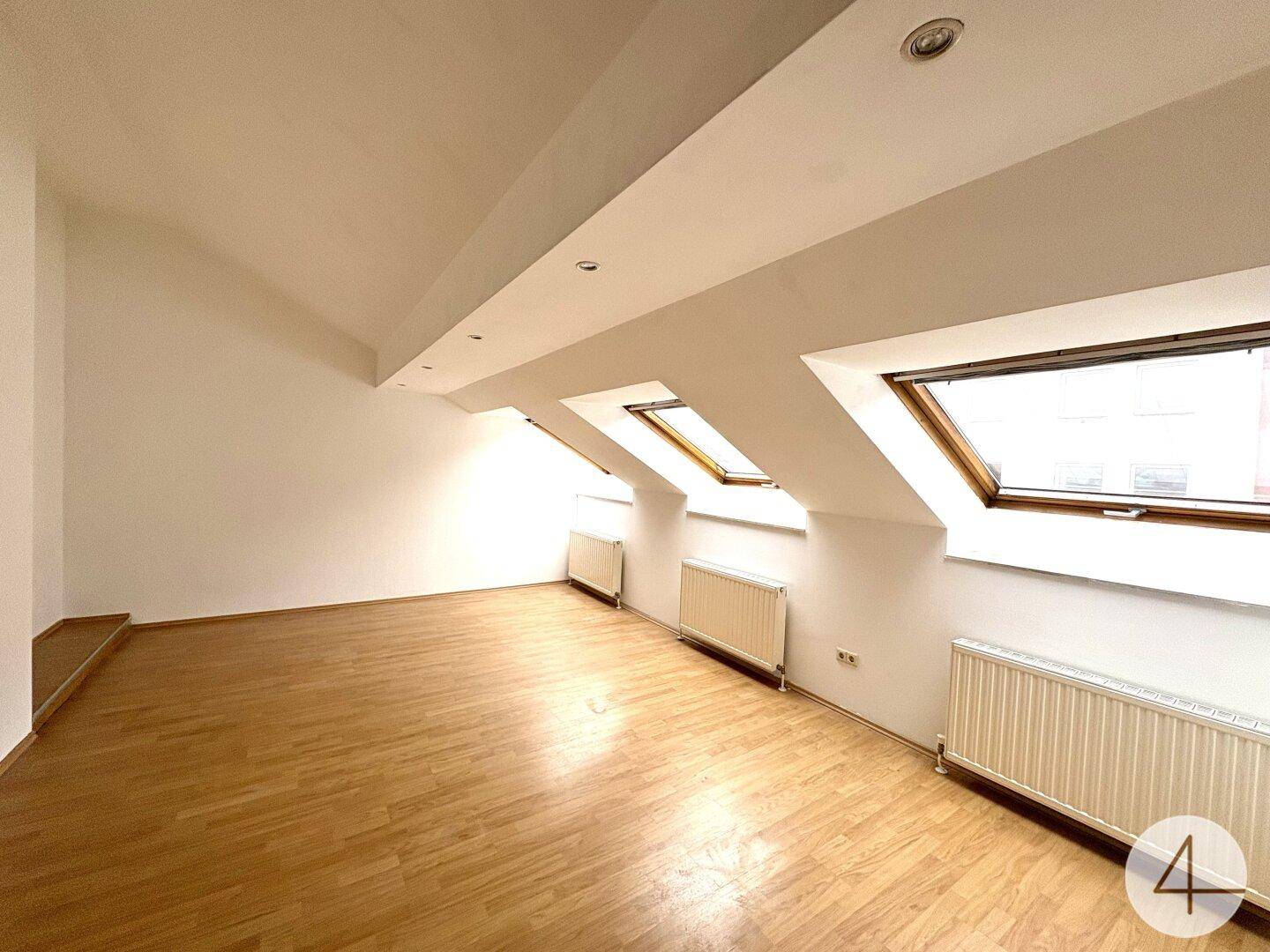 Helles Dachgeschosszimmer mit Holzfußboden, weißen Wänden und drei schrägen Dachfenstern.