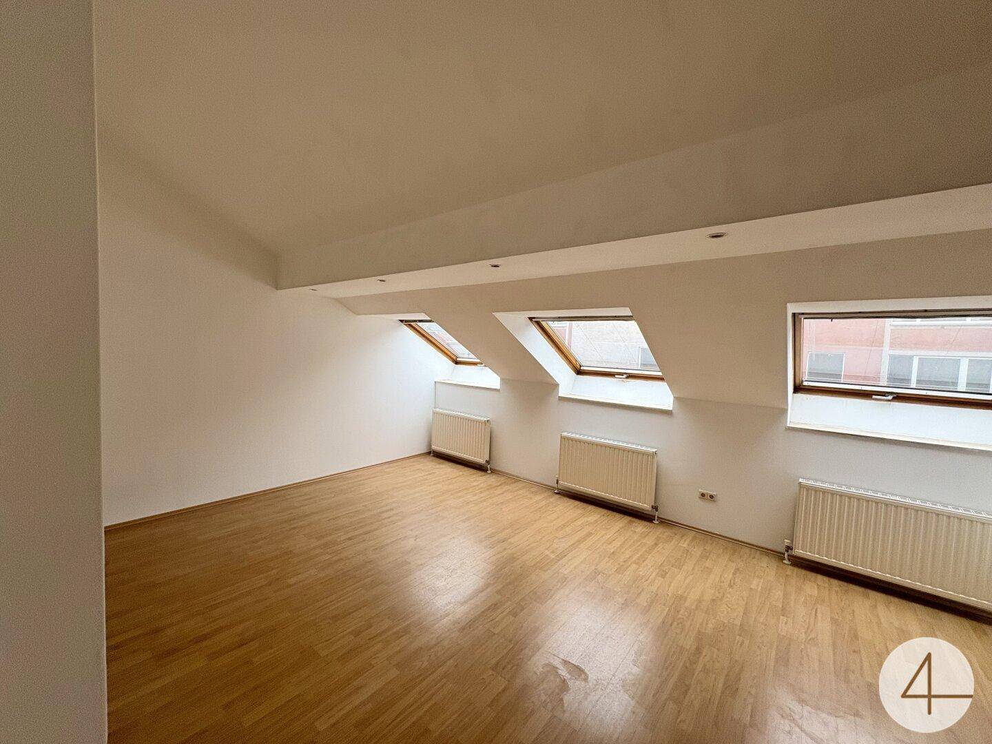 Geräumiges Dachgeschosszimmer mit Holzfußboden, weißen Wänden und drei Dachfenstern.