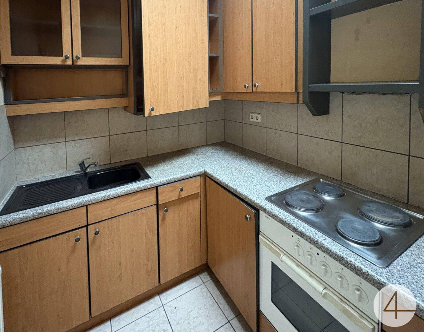 Kleine Küche mit hellbraunen Holzschränken, gefliestem Spritzschutz und einfacher Ausstattung.