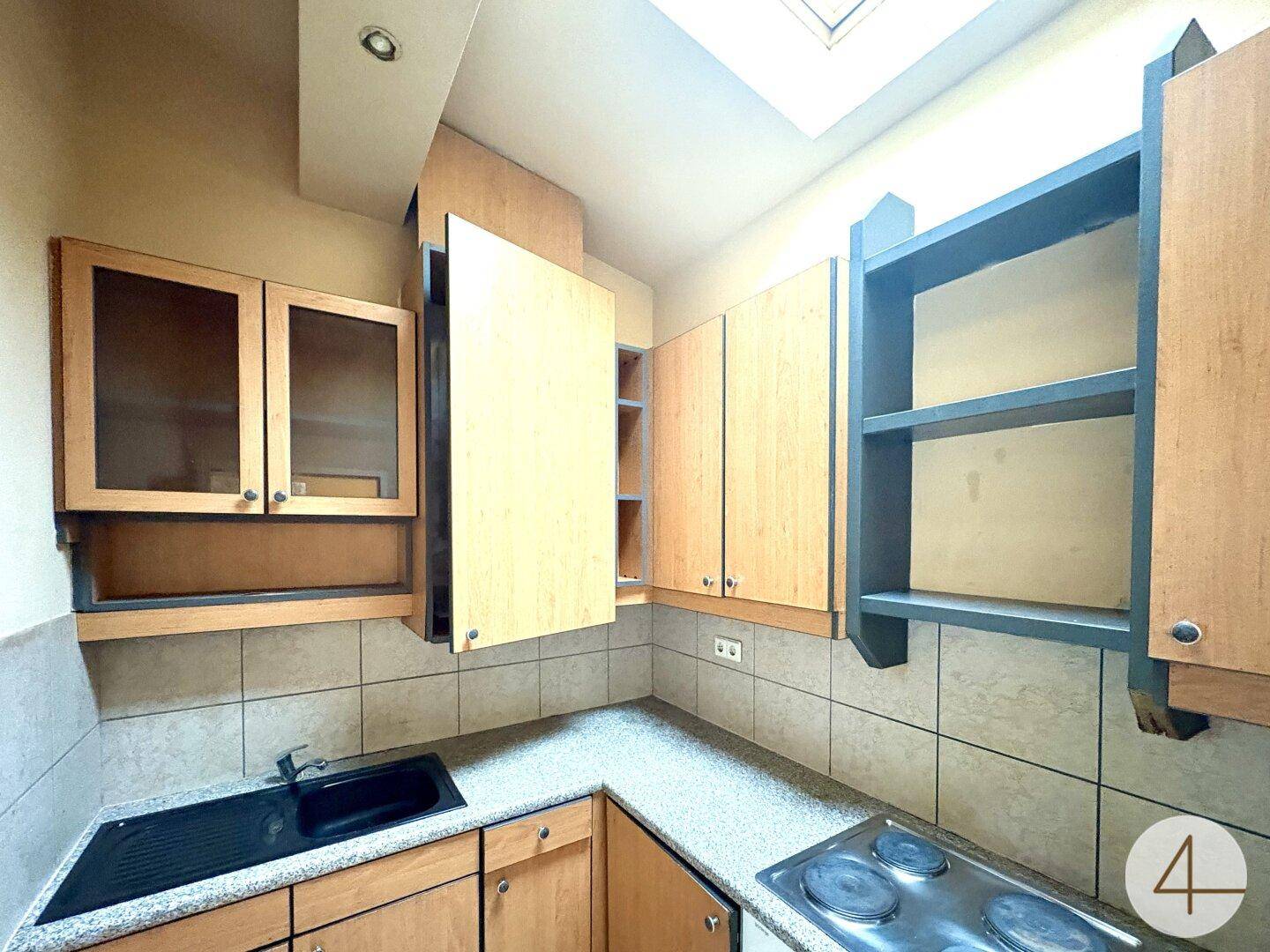 Detailansicht der Küche mit Spüle, Herd und Holzschränken unter einem Dachfenster.