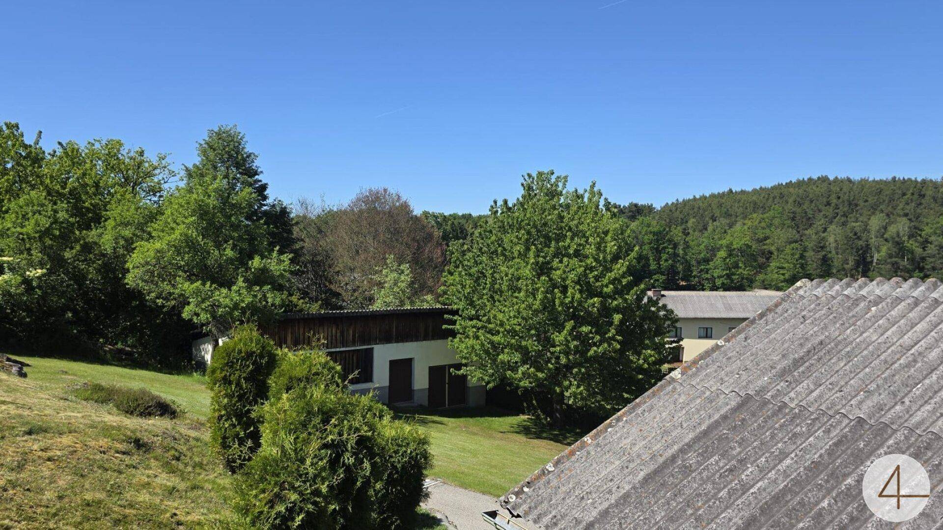 Weitläufige grüne Landschaft mit Bäumen und Häusern unter einem klaren blauen Himmel.