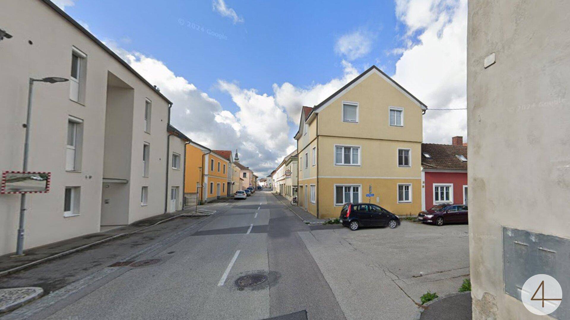 Blick auf eine ruhige Wohnstraße mit dem gelben Gebäude und weiteren Häusern unter blauem Himmel.