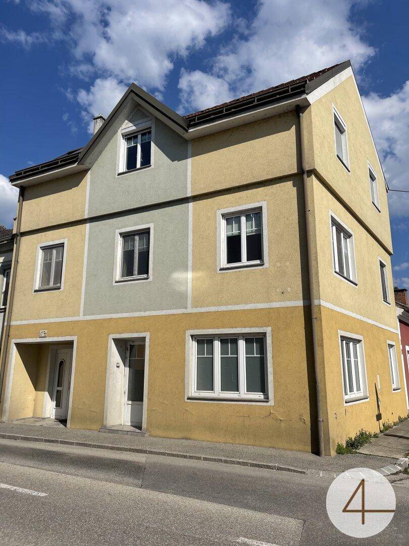 Ansicht des mehrstöckigen Gebäudes mit gelb-grauer Fassade und weißen Fenstern unter blauem Himmel.