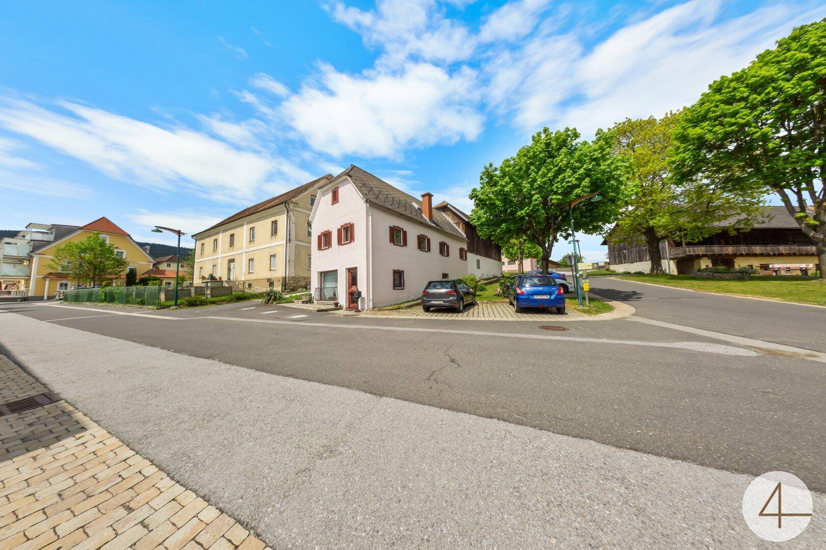 Ansicht des Gebäudes von der Straße mit parkenden Autos und umliegender Bebauung.