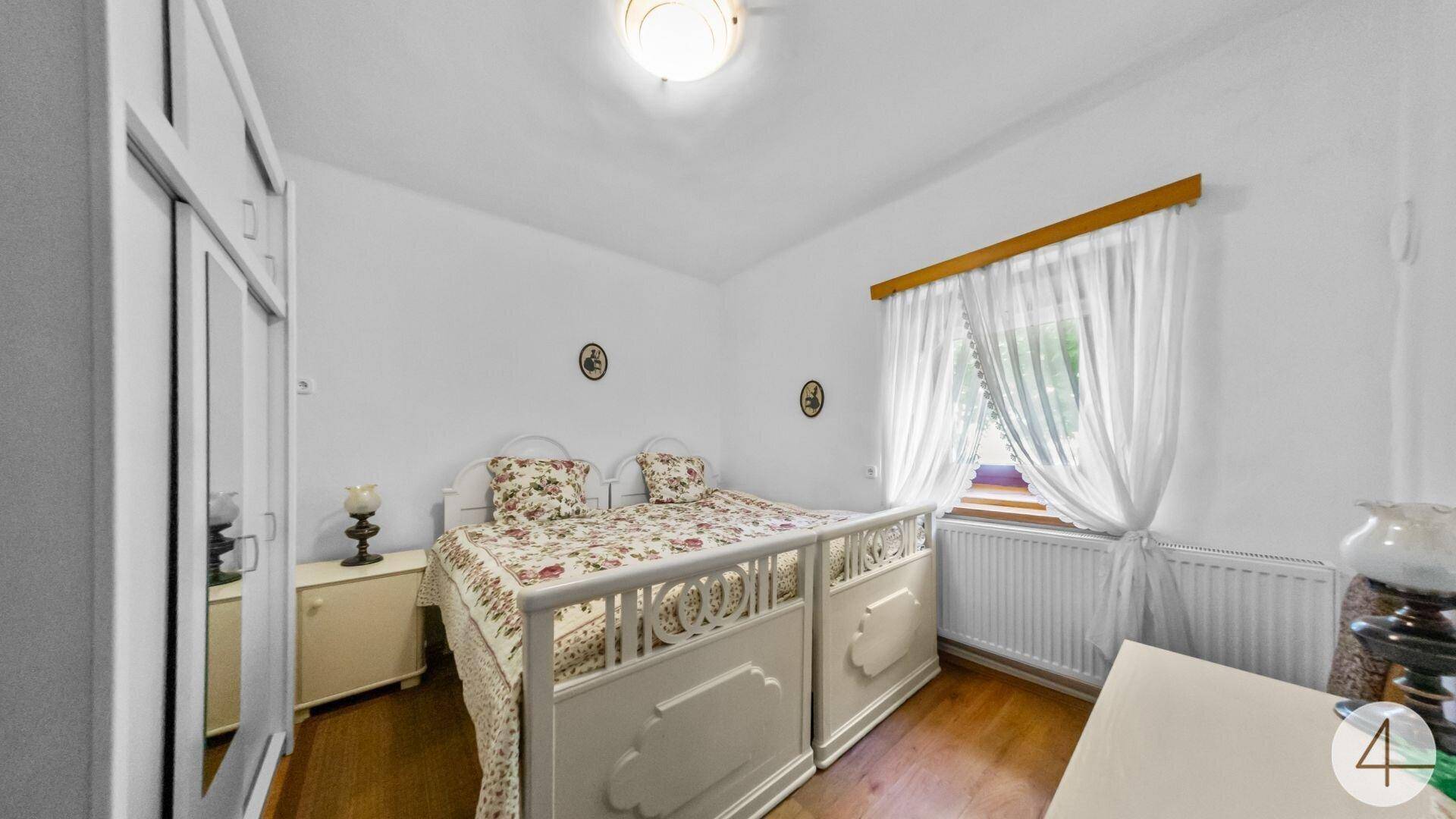 Helles Schlafzimmer mit weißem Bett, floraler Bettwäsche und einem Kleiderschrank mit Spiegeltüren.