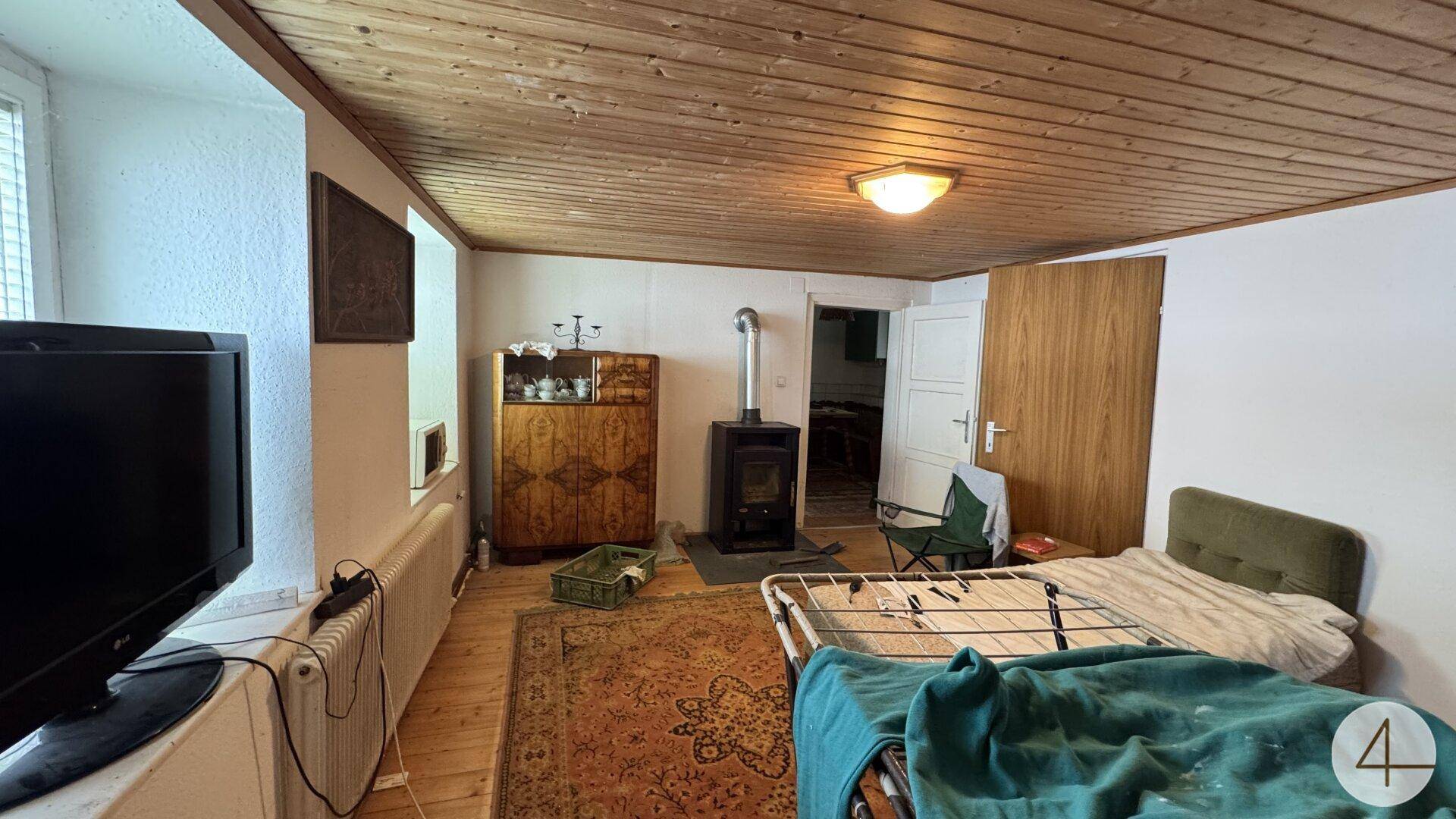Gemütliches Zimmer mit Holzdecke, Holzofen, Bett und Heizkörper.