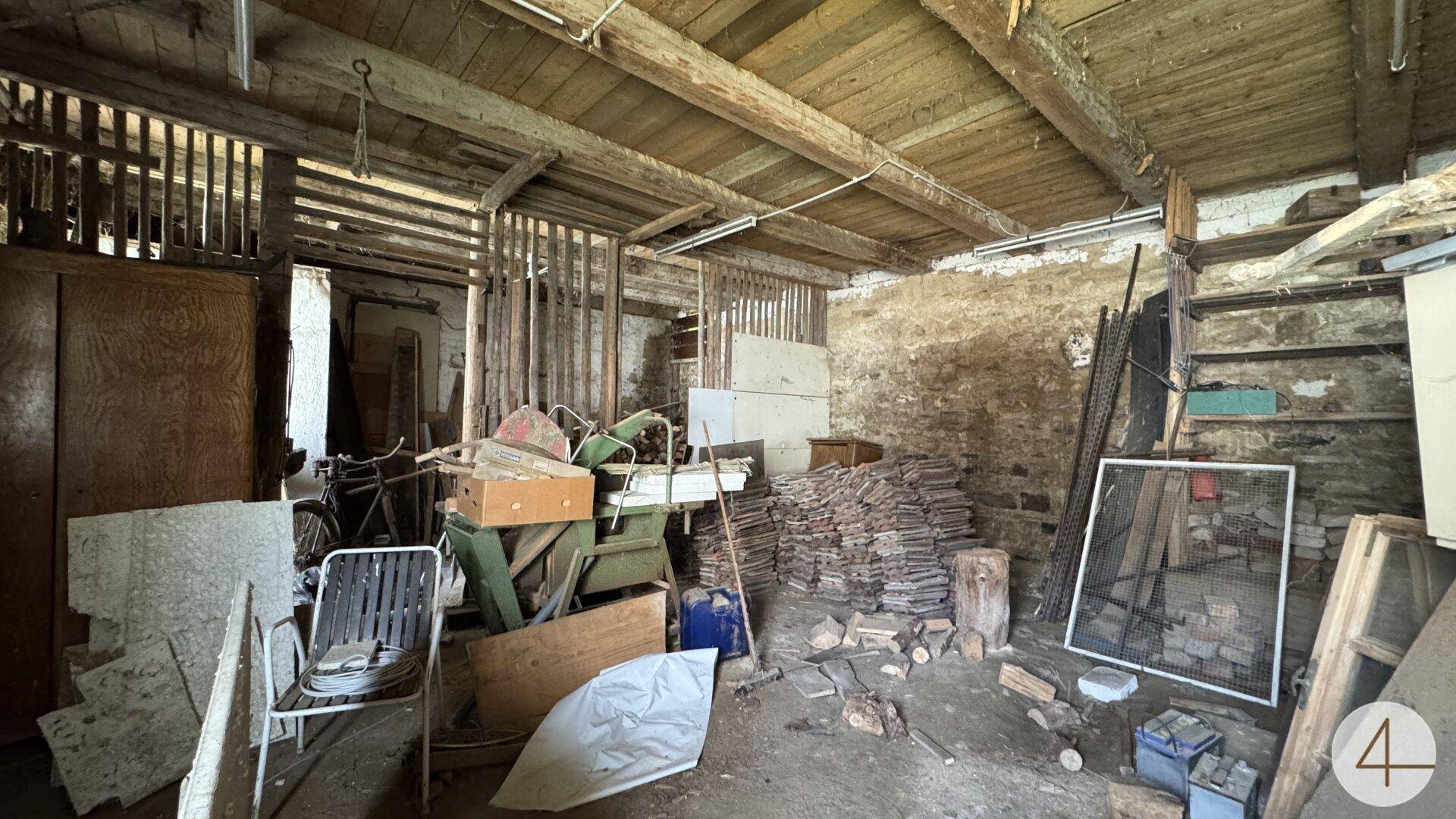 Unaufgeräumter Raum mit sichtbaren Holzstrukturen, Ziegelwänden und gelagerten Baumaterialien.