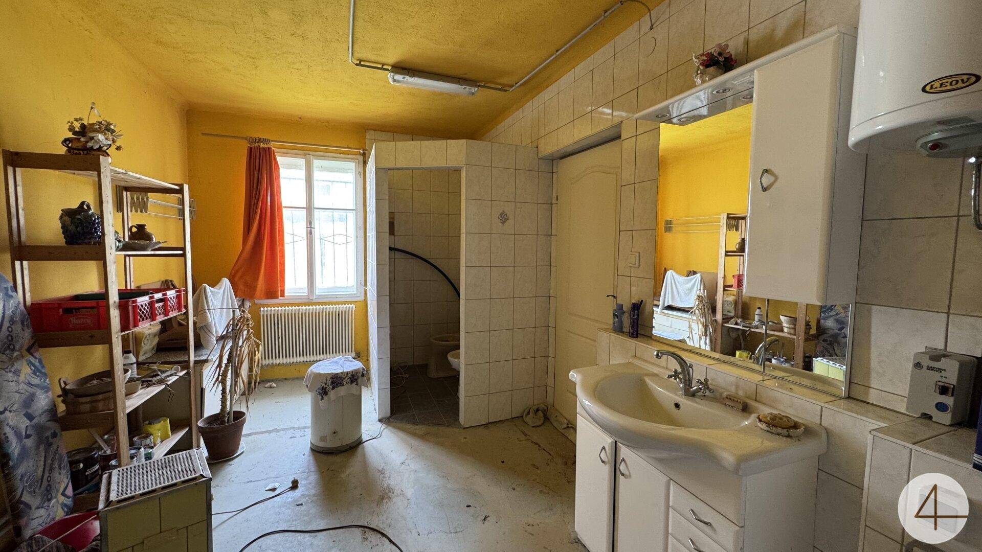 Veraltetes Badezimmer mit gelben Wänden, weißen Fliesen, Waschbecken und separater Toilette.