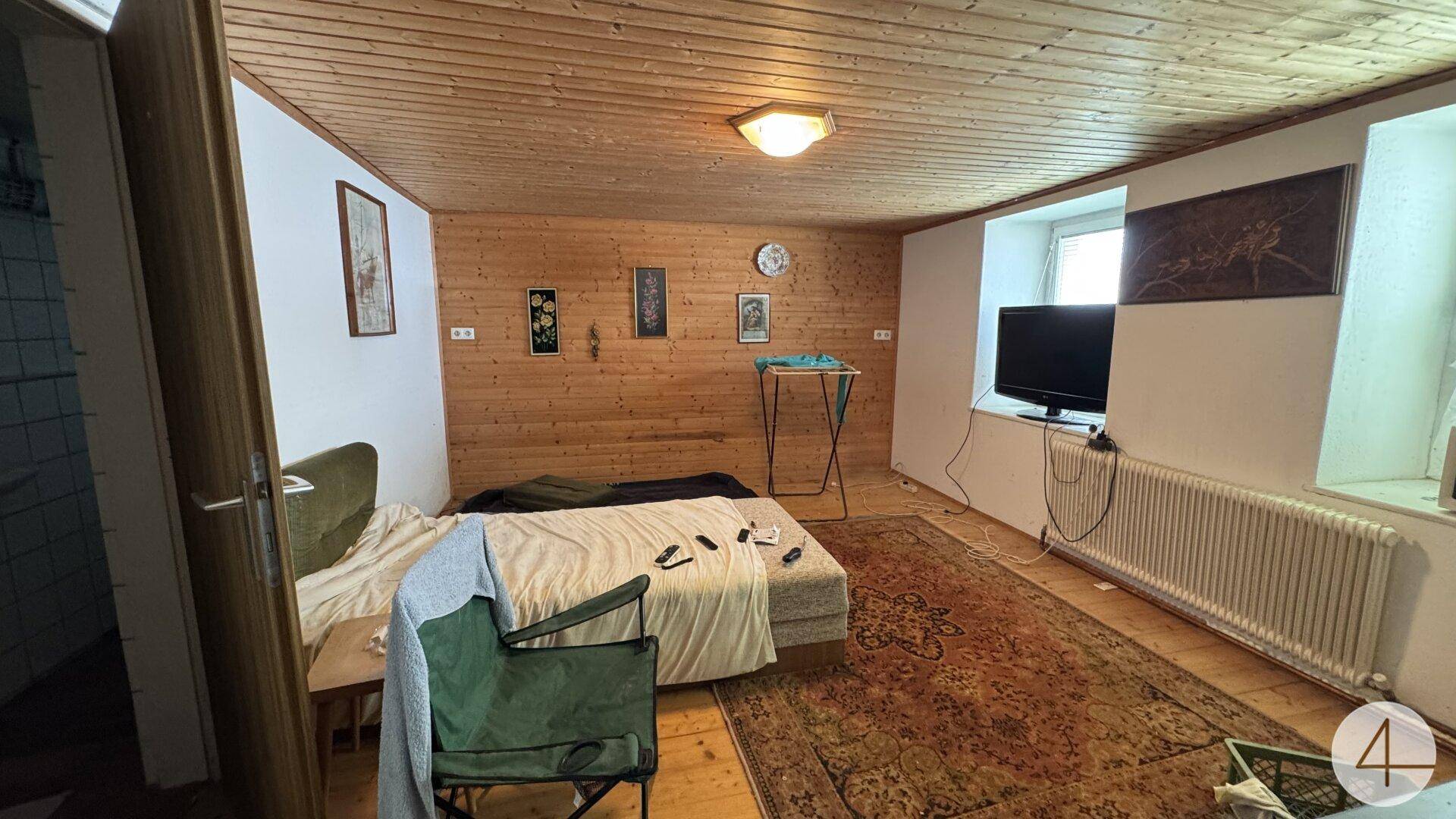 Schlafzimmer mit holzvertäfelten Wänden und Decke, Bett und Fernseher.