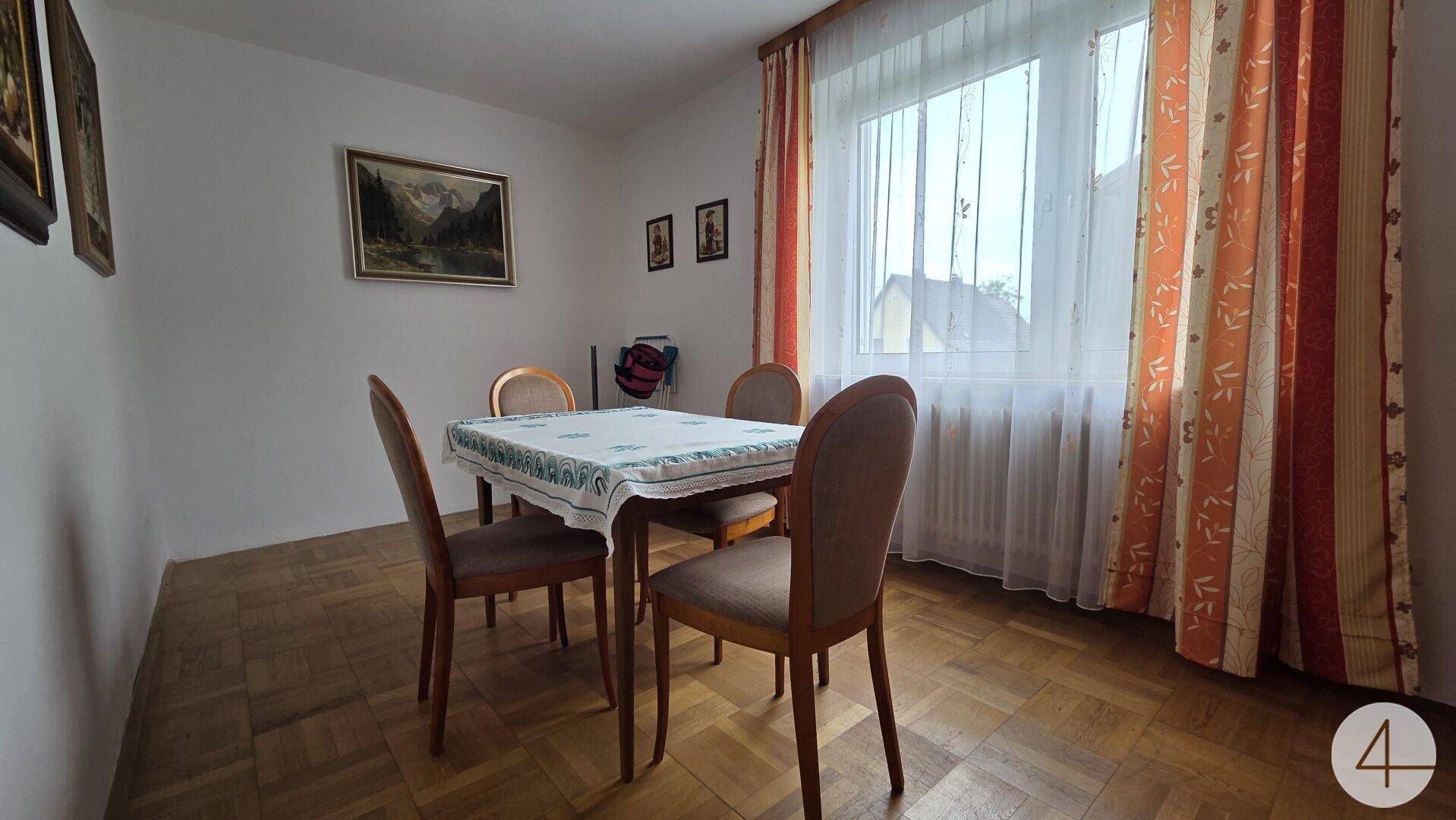 Esszimmer mit Holztisch, Stühlen und einem großen Fenster, das viel Tageslicht hereinlässt.