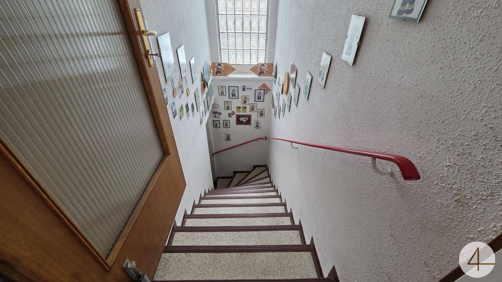 Treppenhaus mit Handlauf, Fliesenstufen und einer Wanddekoration aus vielen gerahmten Bildern.