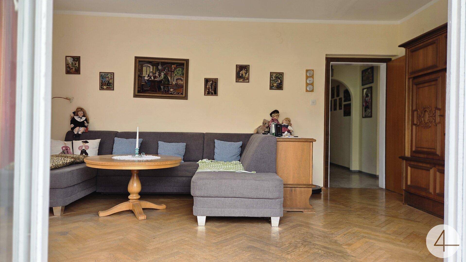 Wohnzimmer mit bequemer Couch, Holztisch und traditioneller Dekoration an den Wänden, die Gemütlichkeit ausstrahlt.