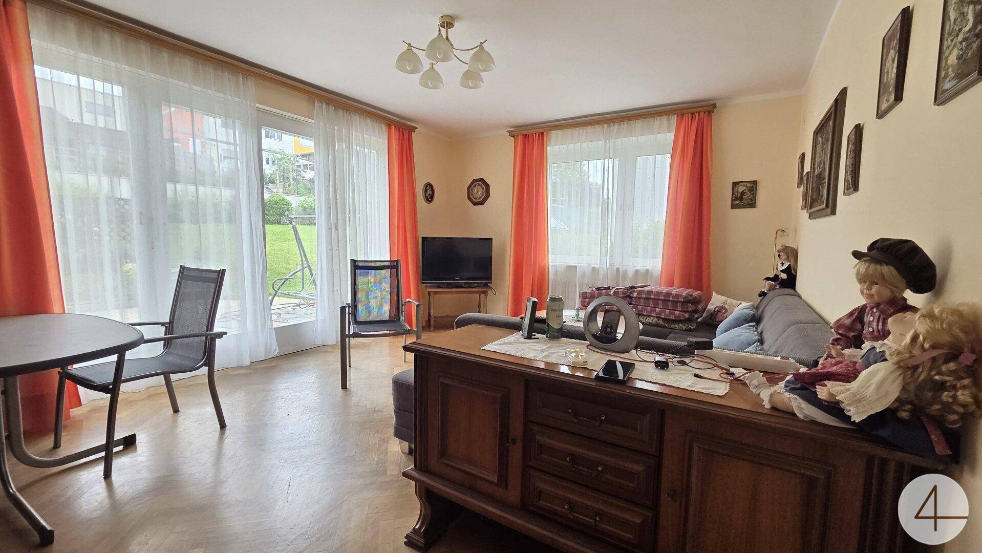 Helles Wohnzimmer mit Parkettboden, großem Fenster und traditionellen Möbeln, die eine warme Atmosphäre schaffen.