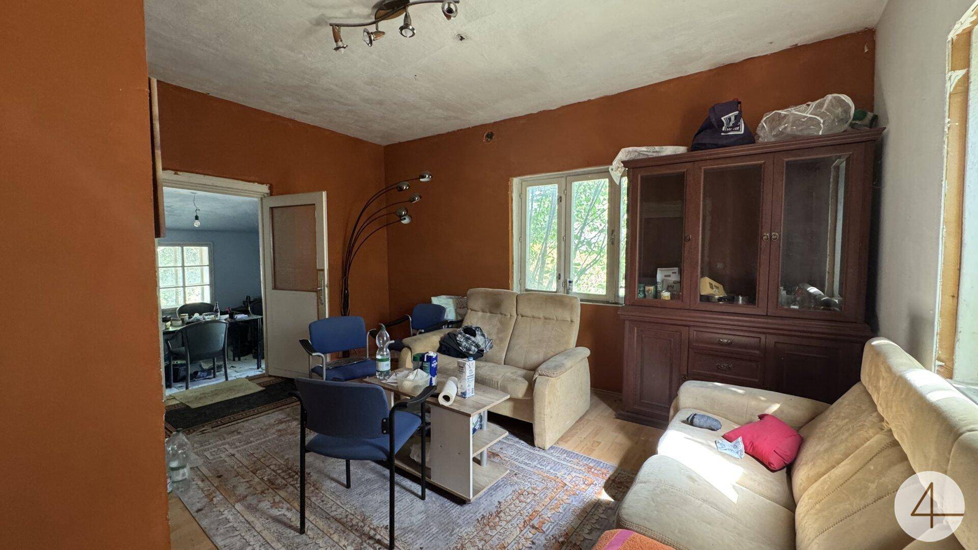 Gemütliches Wohnzimmer mit bequemen Sofas, einem Holzschrank und Blick in einen angrenzenden Raum.