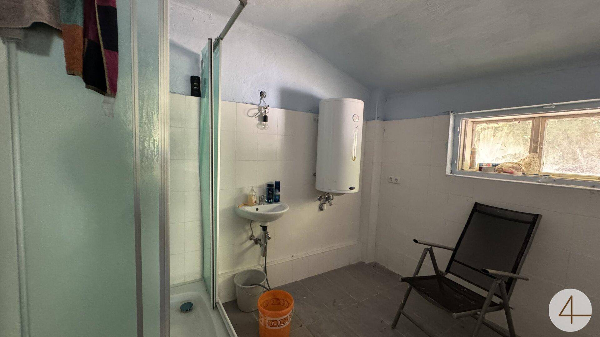 Funktionales Badezimmer mit Duschkabine, kleinem Waschbecken und Warmwasserboiler.