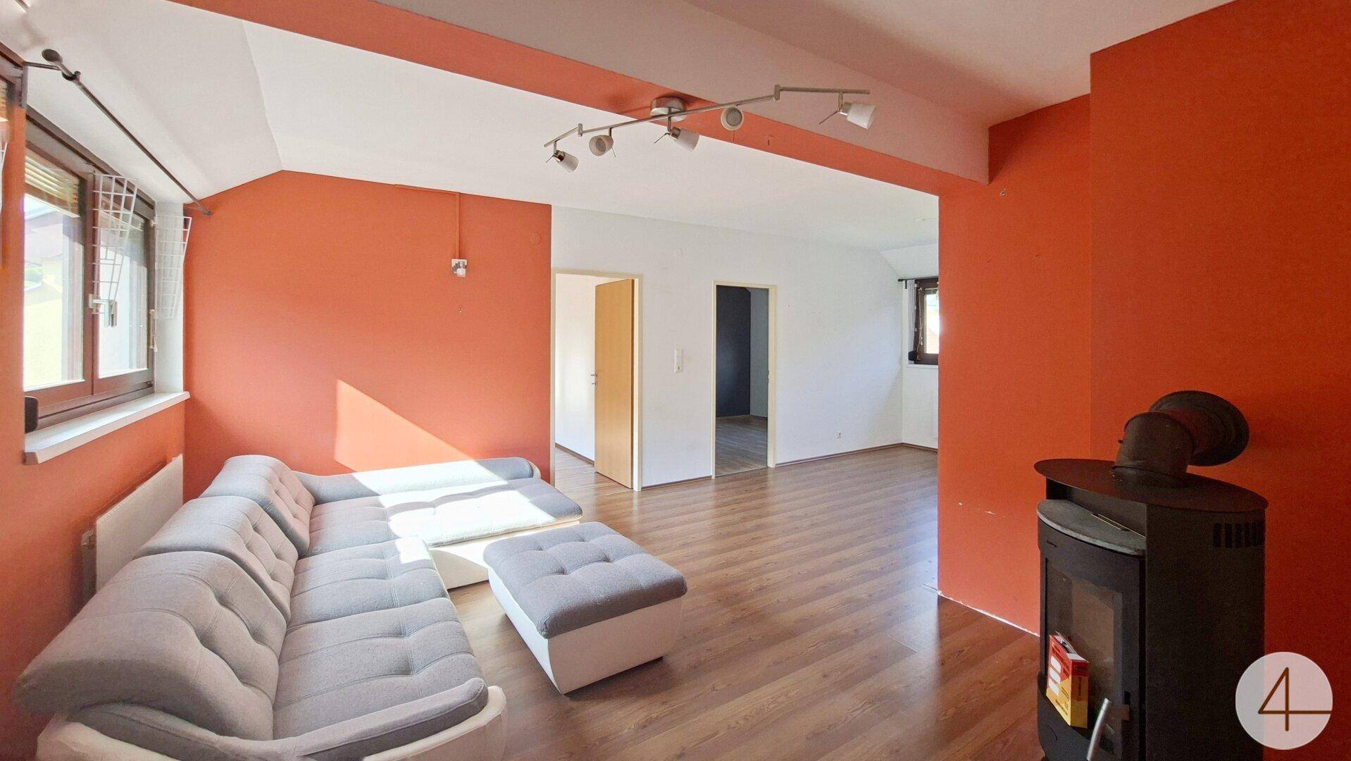 Helles Wohnzimmer mit modernem Kaminofen, Laminatboden und orangefarbenen Akzentwänden.