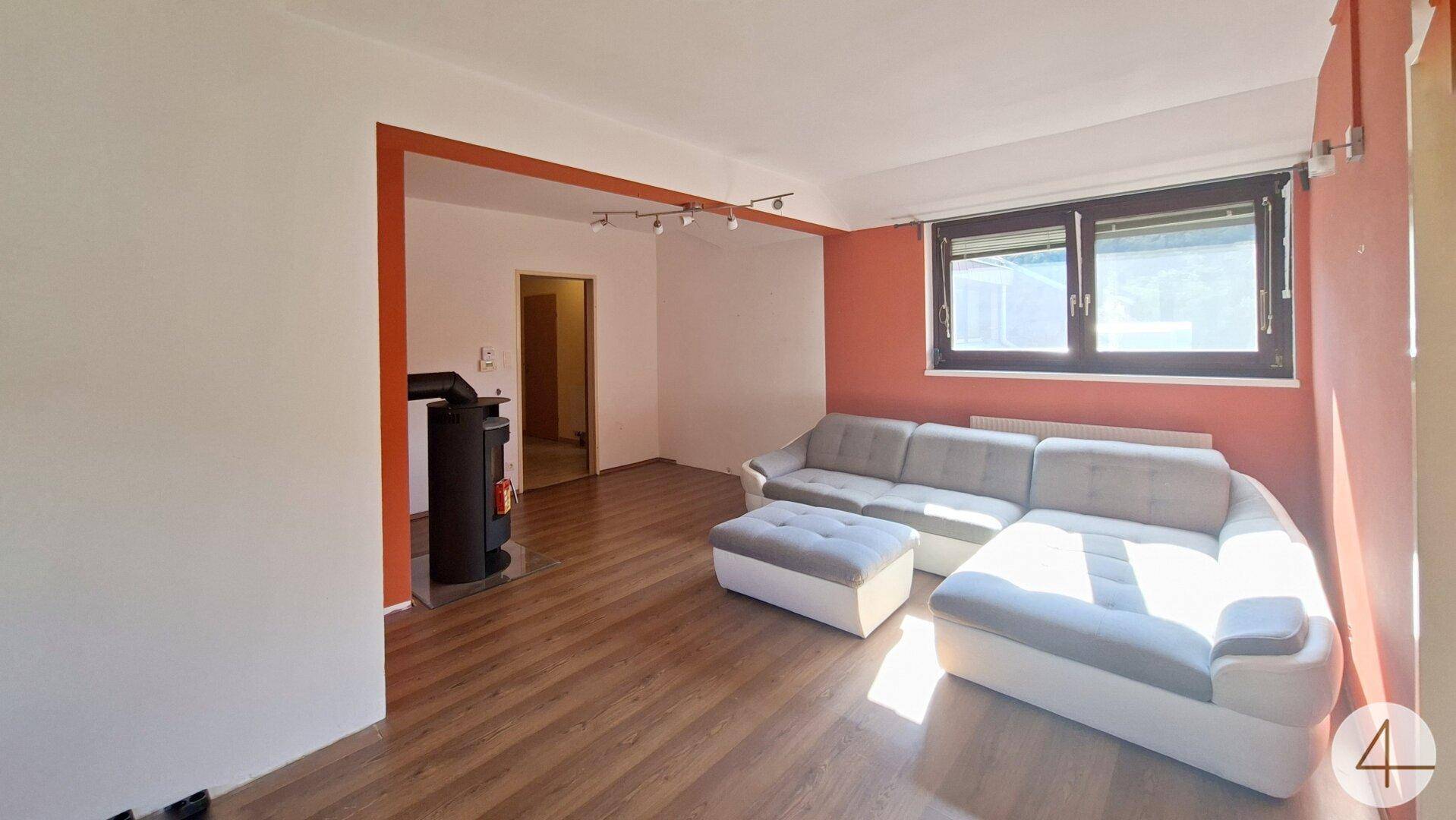 Geräumiges Wohnzimmer mit gemütlichem Sofa, Kaminofen und großen Fenstern für viel Tageslicht.