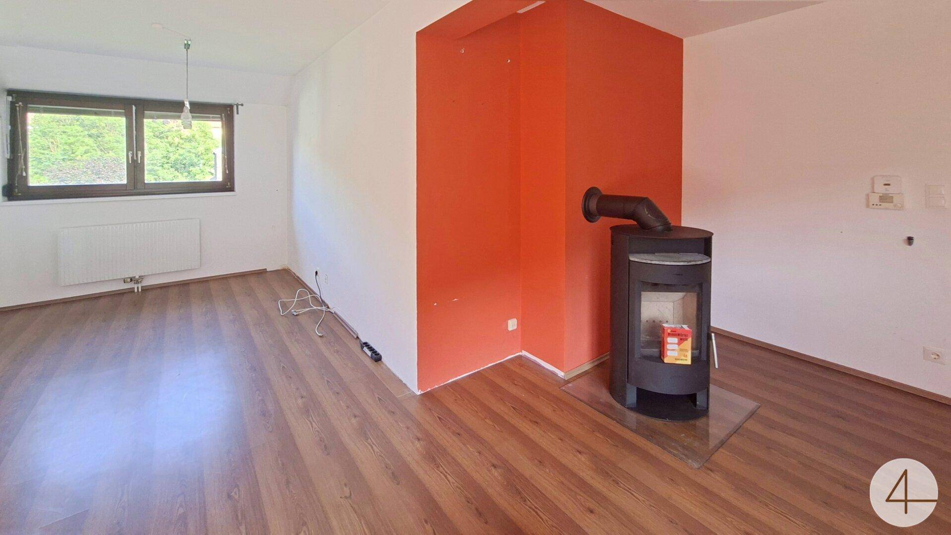 Heller Wohnbereich mit Kaminofen und Laminatboden, ideal für gemütliche Abende.