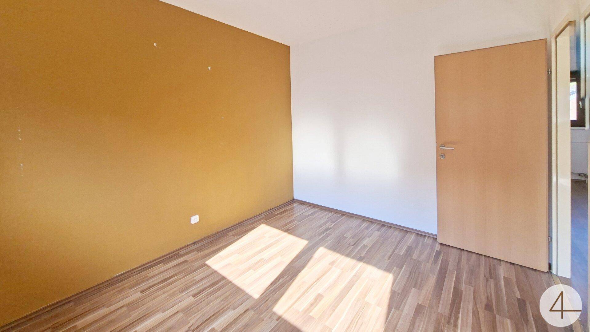 Helles Schlafzimmer mit Laminatboden und einer sonnigen gelben Akzentwand.