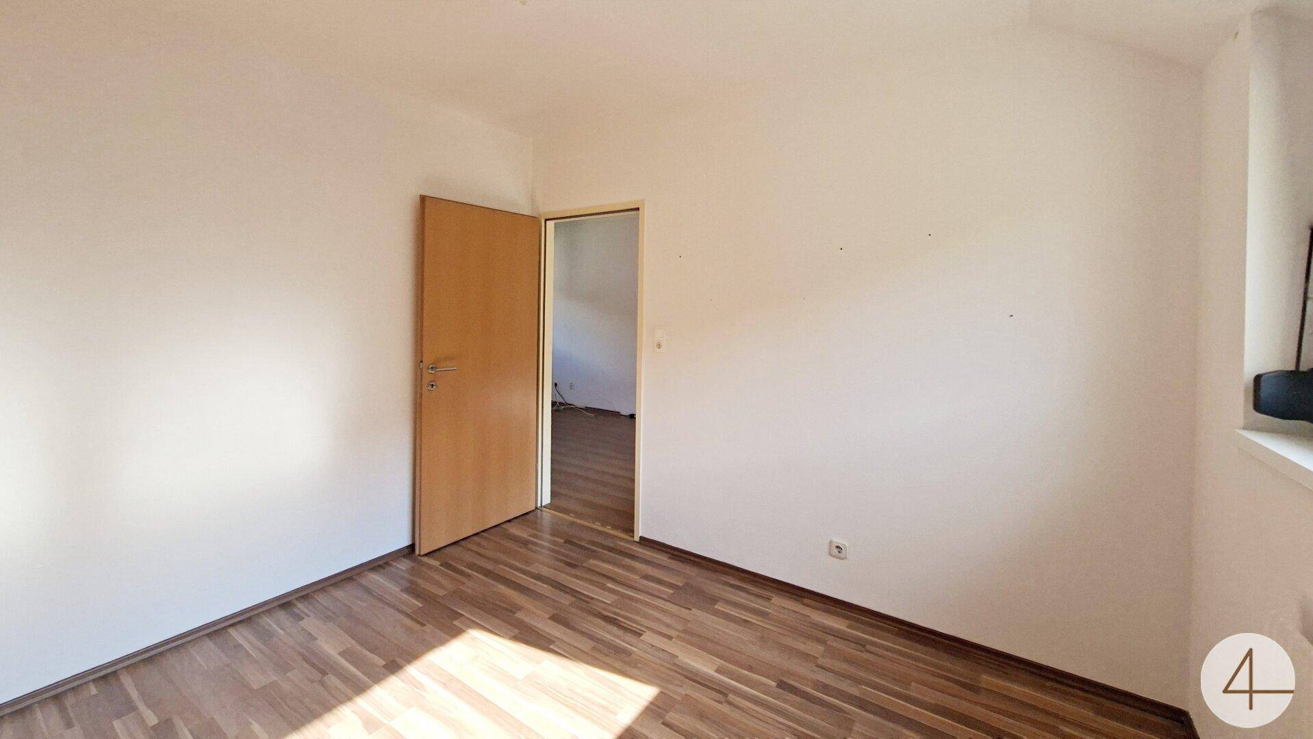 Schlafzimmer mit Laminatboden und weiß gestrichenen Wänden, ideal für ein Kinderzimmer oder Büro.