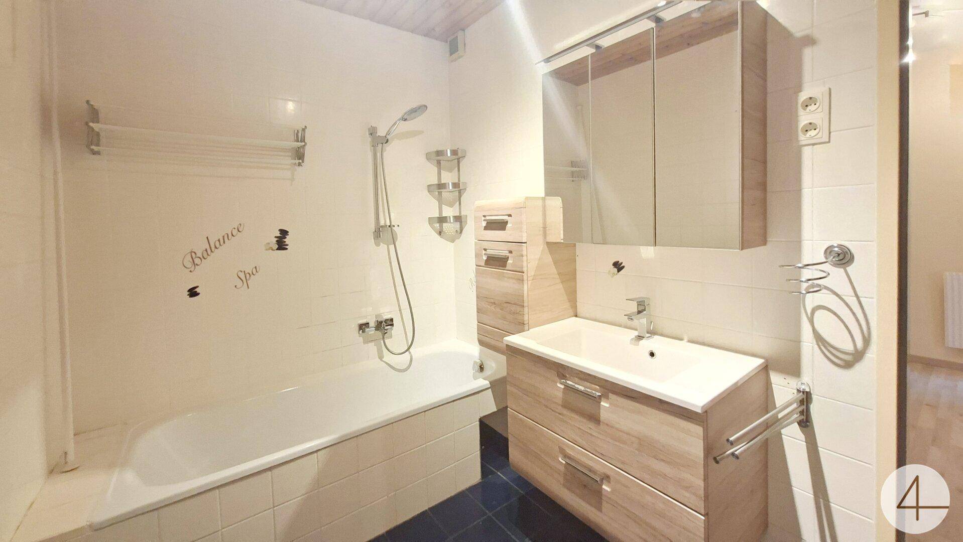 Badezimmer mit Badewanne, Duschfunktion, Waschtischunterschrank und Spiegelschrank.