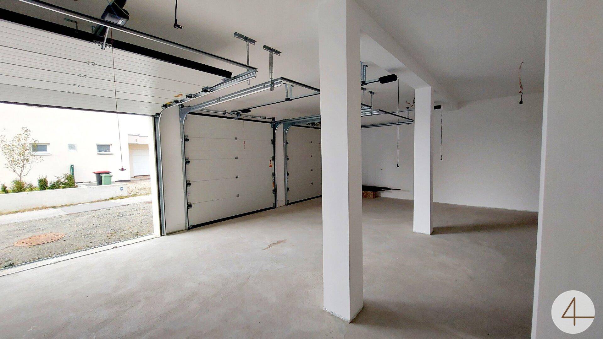 Geräumige Doppelgarage mit zwei geöffneten Toren, Betonboden und tragenden Säulen.