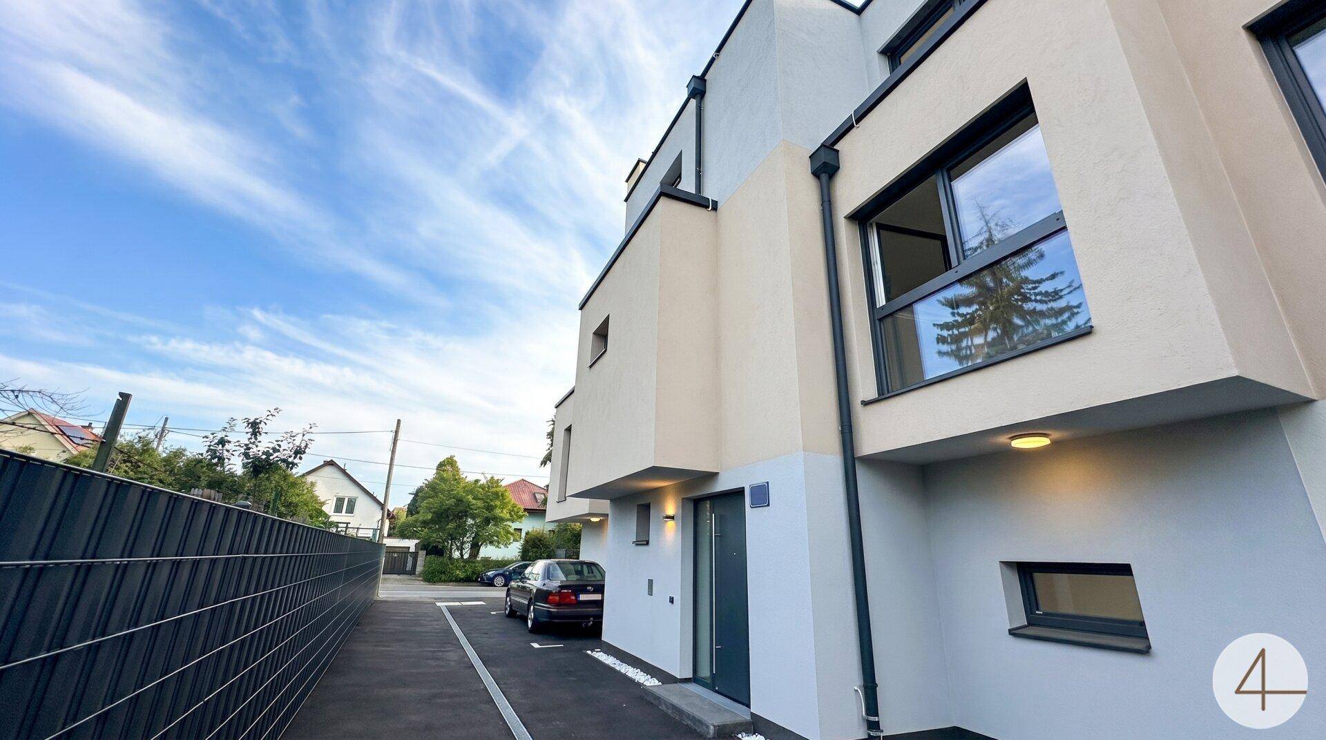 Moderne Gebäudefassade mit klaren Linien, großen Fenstern und einem Stellplatz vor dem Eingang.