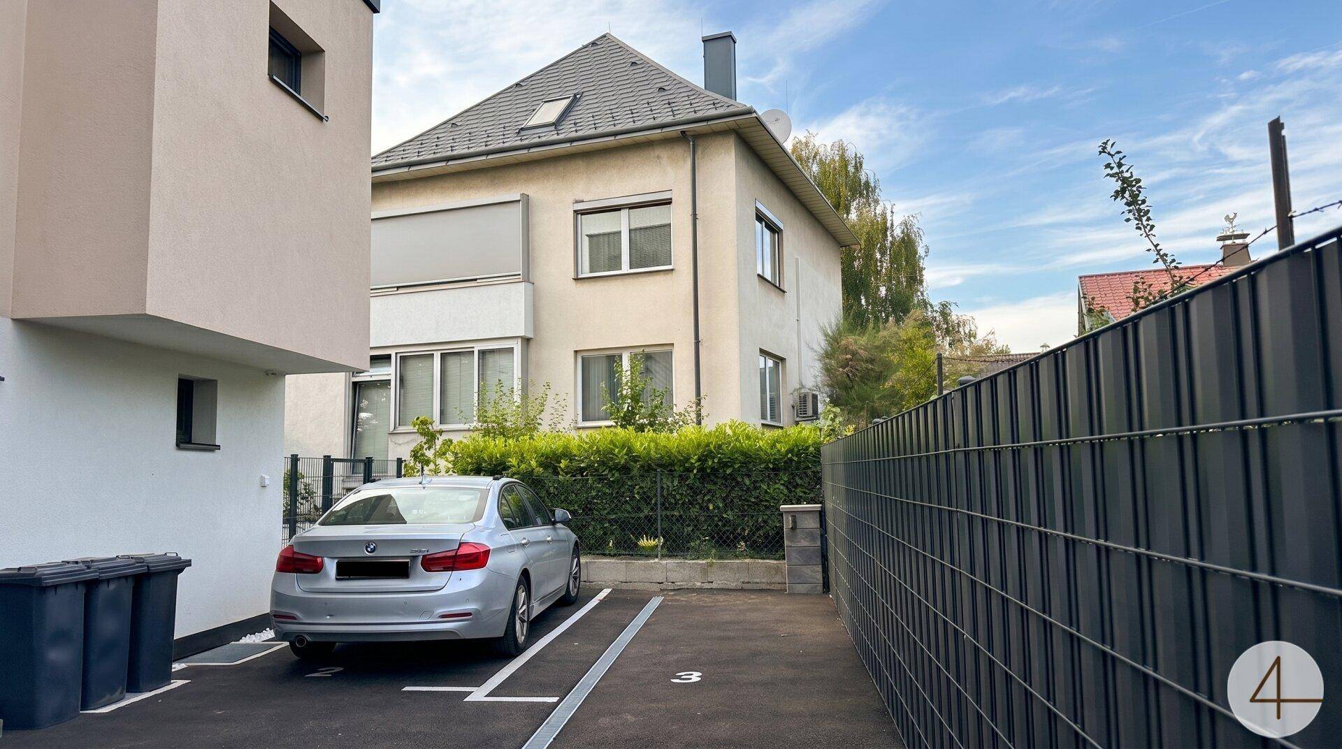 Außenansicht mit einem gepflasterten Stellplatz und einem älteren Gebäude im Hintergrund.