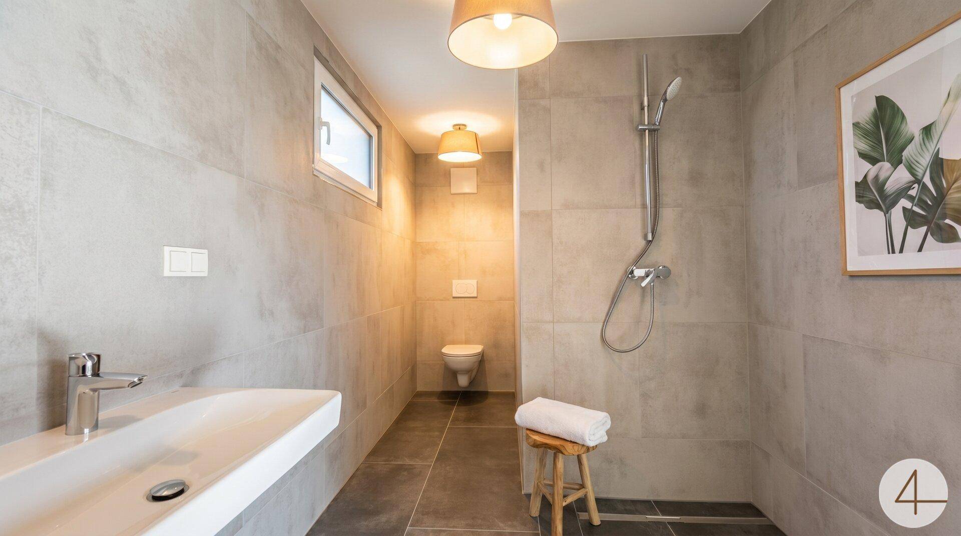 Modernes Badezimmer mit ebenerdiger Dusche, Hänge-WC und großformatigen grauen Fliesen.