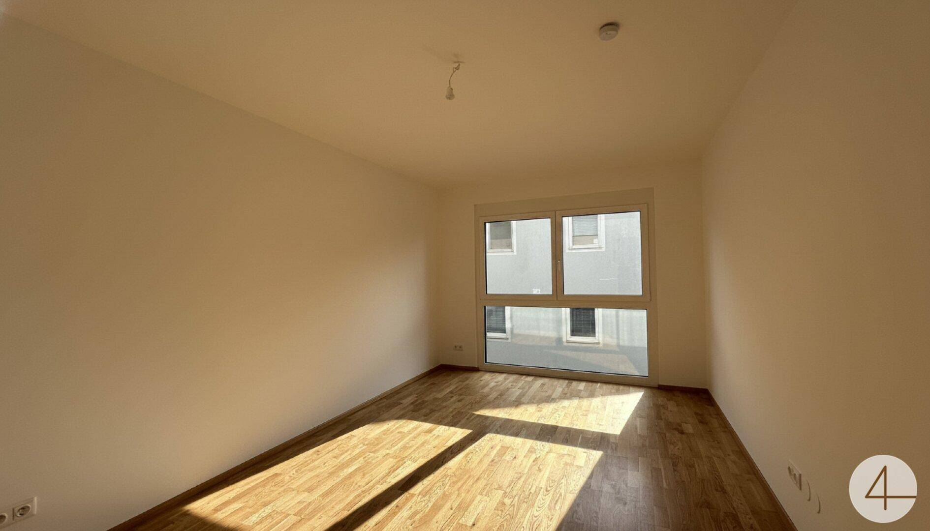Heller Raum mit Holzboden und großem Fenster, das viel Tageslicht hereinlässt.