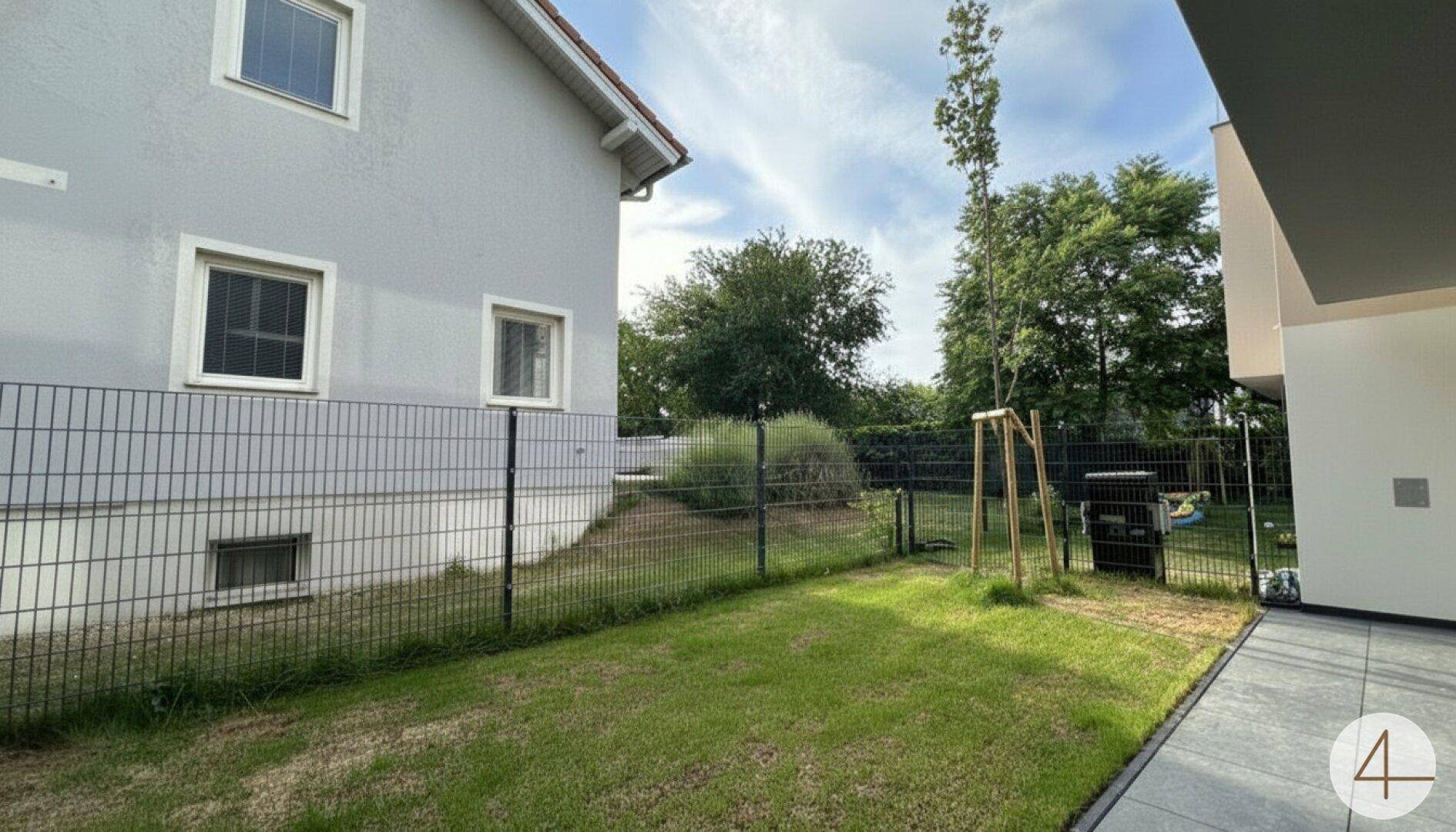 Grüner Gartenbereich mit Rasenfläche und Zaun neben dem Gebäude.