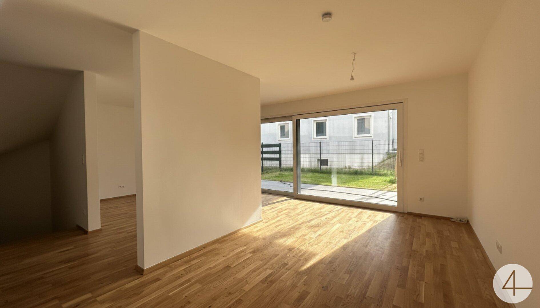 Heller Raum mit Holzboden und großer Schiebetür, die Zugang zum Außenbereich bietet.