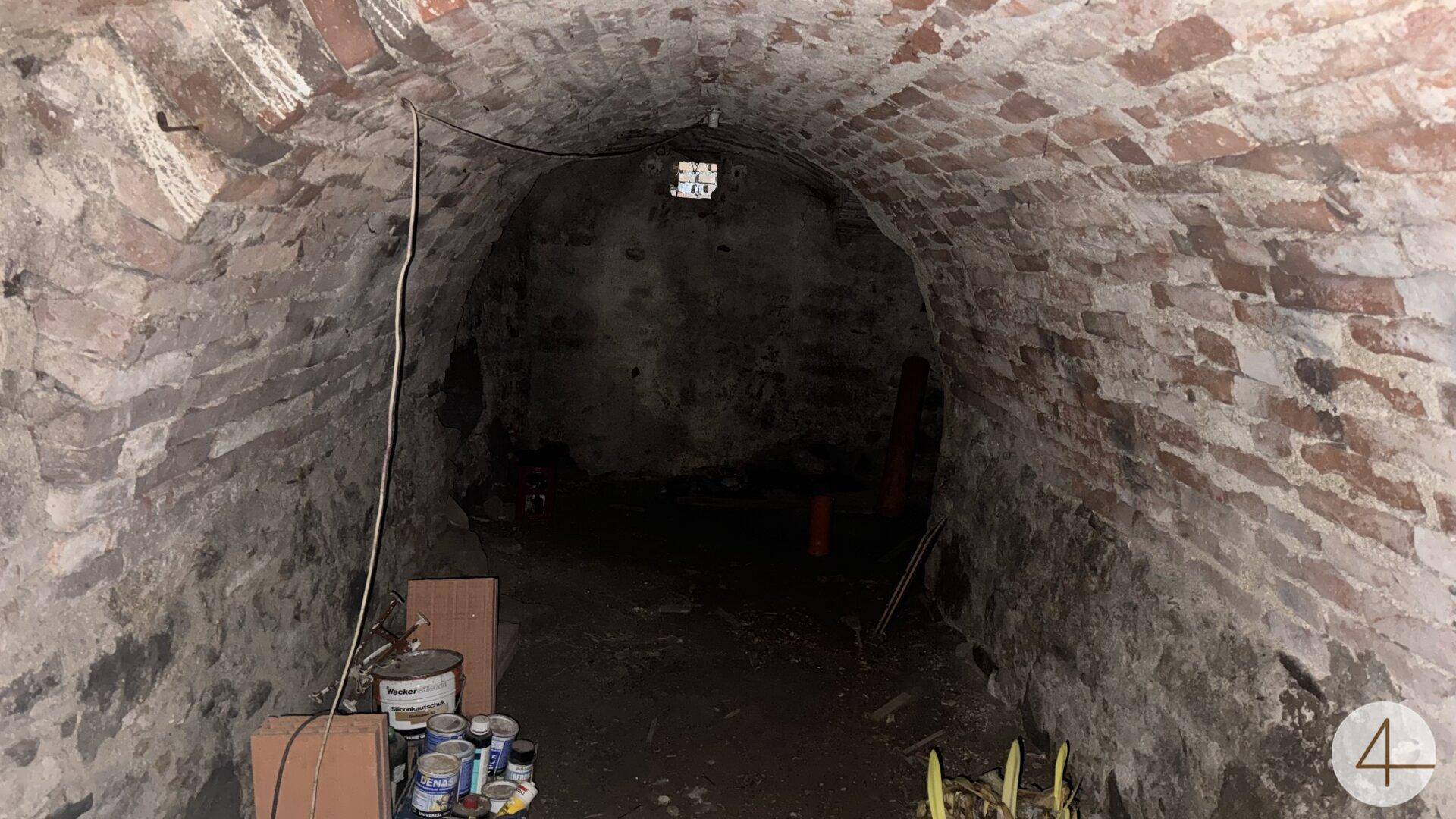 Dunkler, gewölbter Ziegelkeller mit sichtbaren Mauerwerk und begrenzter Beleuchtung.