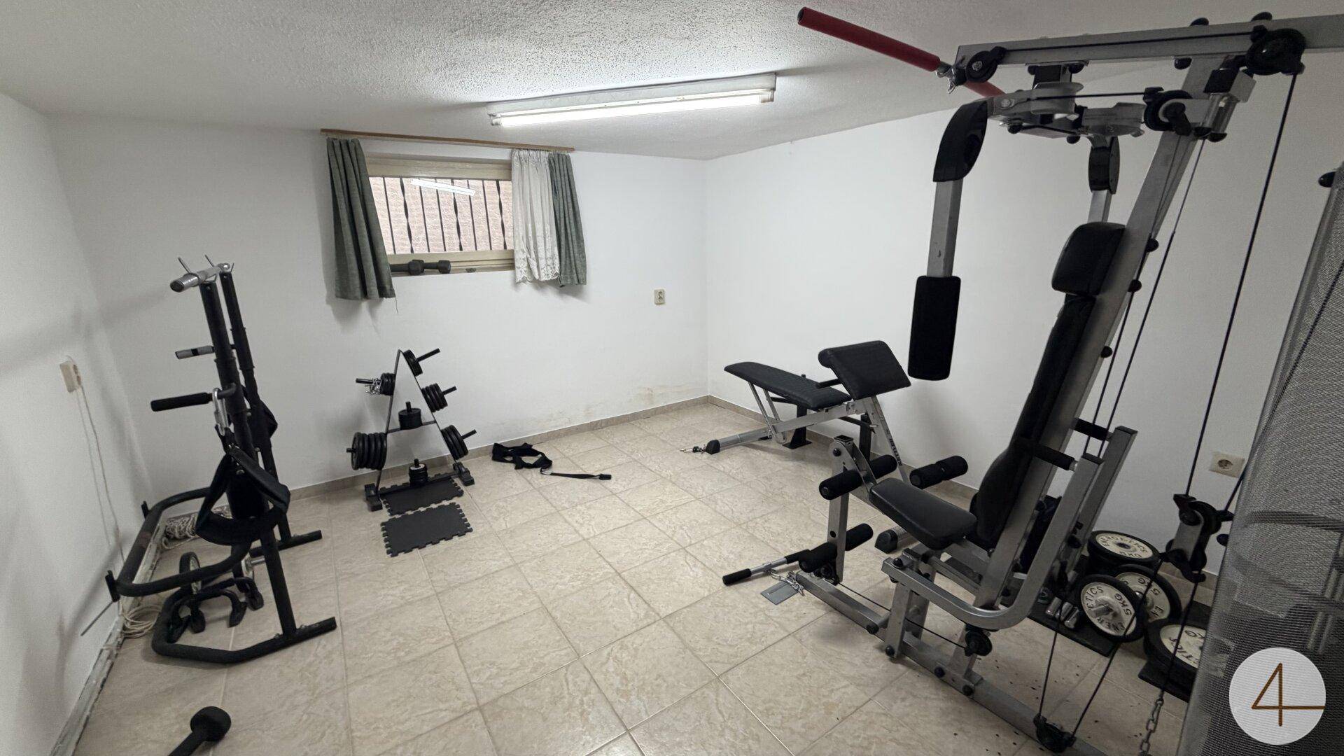 Kellerraum, der als Fitnessraum eingerichtet ist, mit verschiedenen Trainingsgeräten und Fliesenboden.