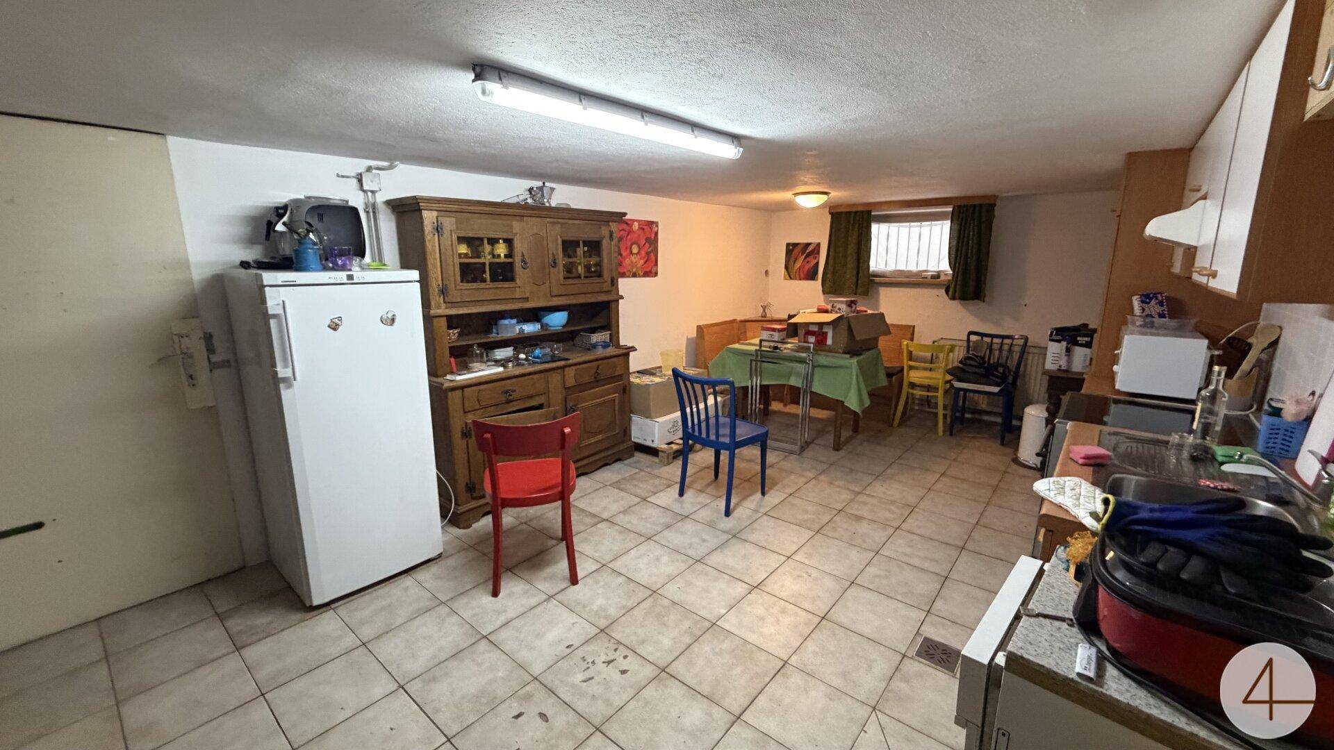 Kellerraum, der als Küche und Essbereich genutzt wird, mit Kühlschrank, Schrank und Esstisch.