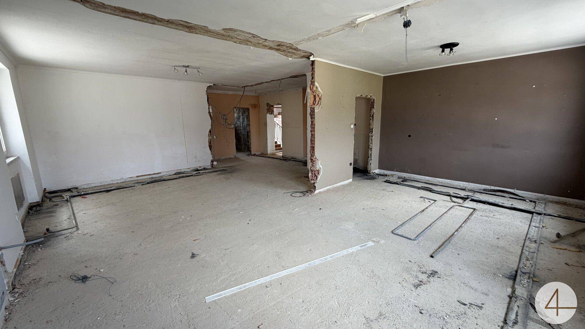 Raum in Renovierung mit freigelegten Wänden, Betonboden und sichtbaren Installationen.