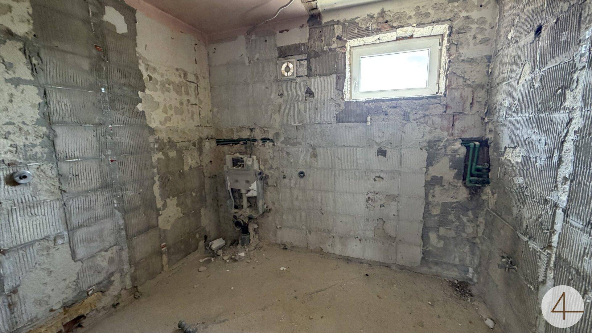 Badezimmer in Renovierung mit freigelegten Wänden, sichtbaren Rohren und einem Fenster.