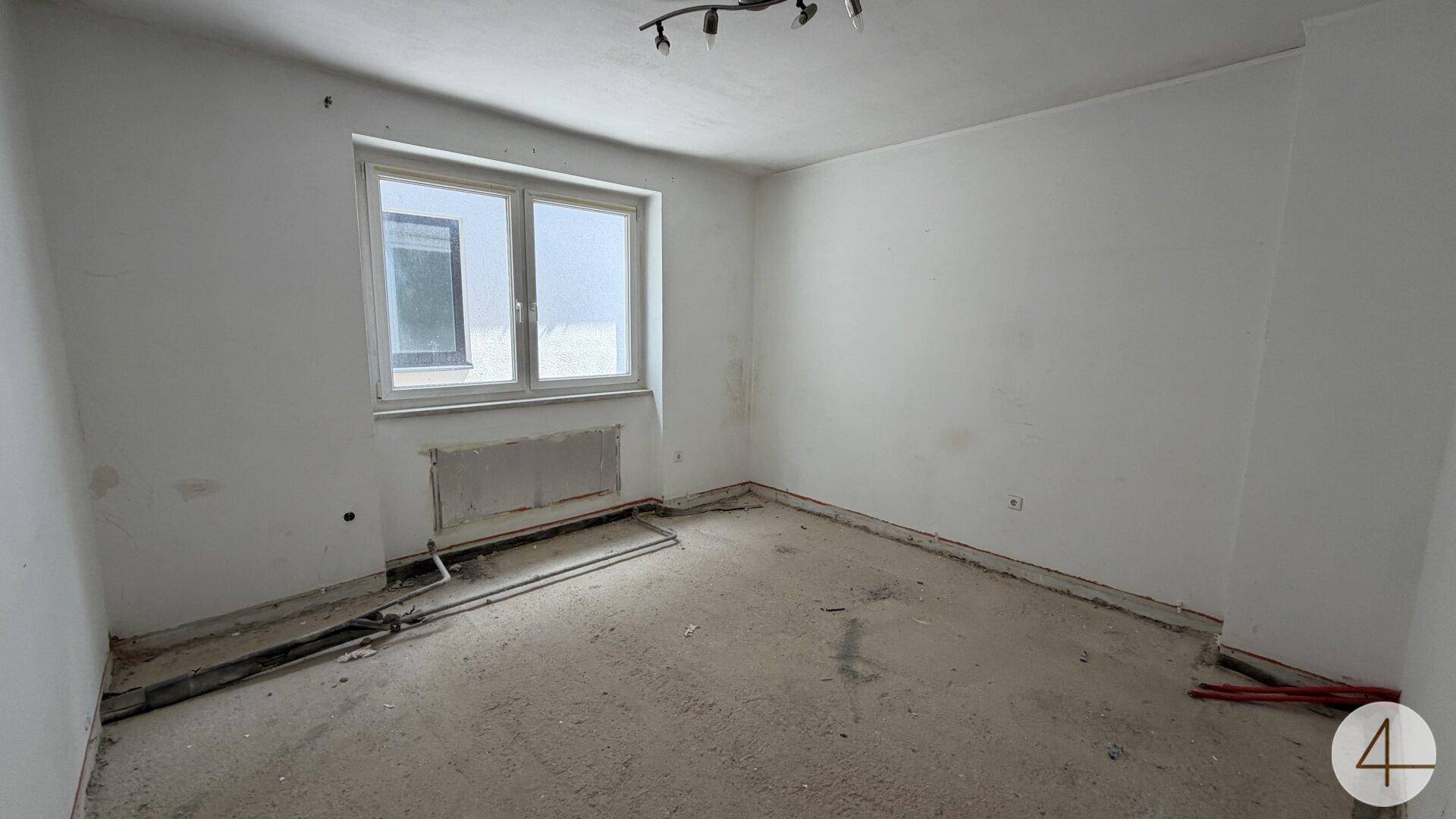 Raum in Renovierung mit einem großen Fenster und einem Betonboden.