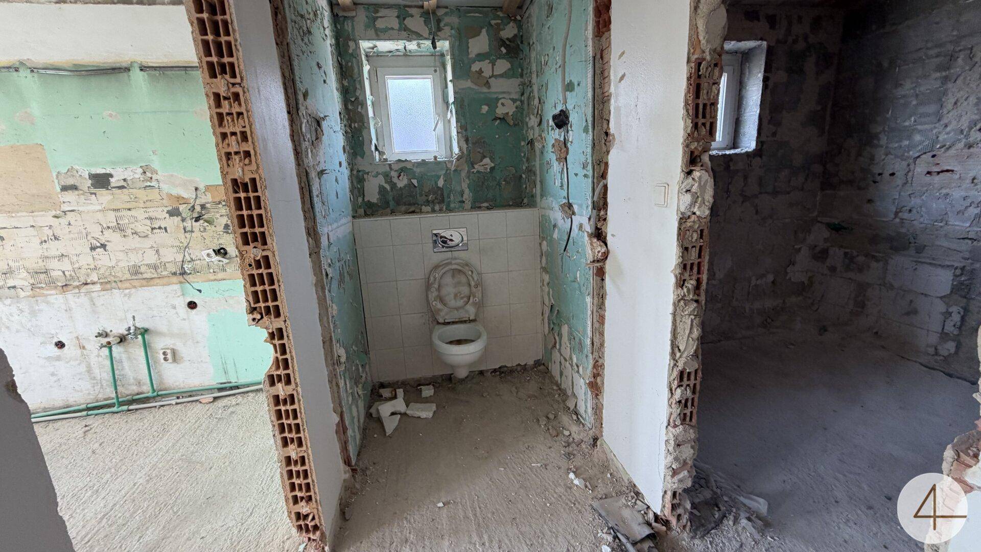 WC-Raum in Renovierung mit Toilette und freigelegten Wänden.