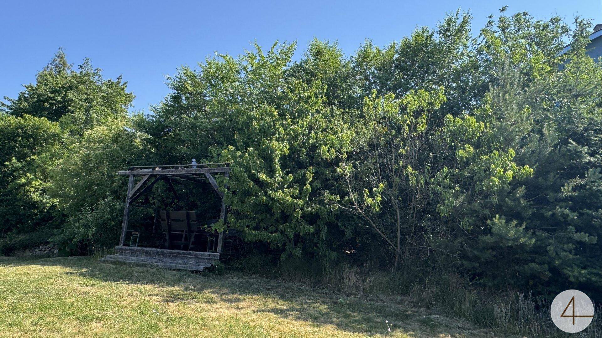 Grüner Garten mit dichtem Baumbestand und einem Holzpavillon, der zum Verweilen im Schatten einlädt.
