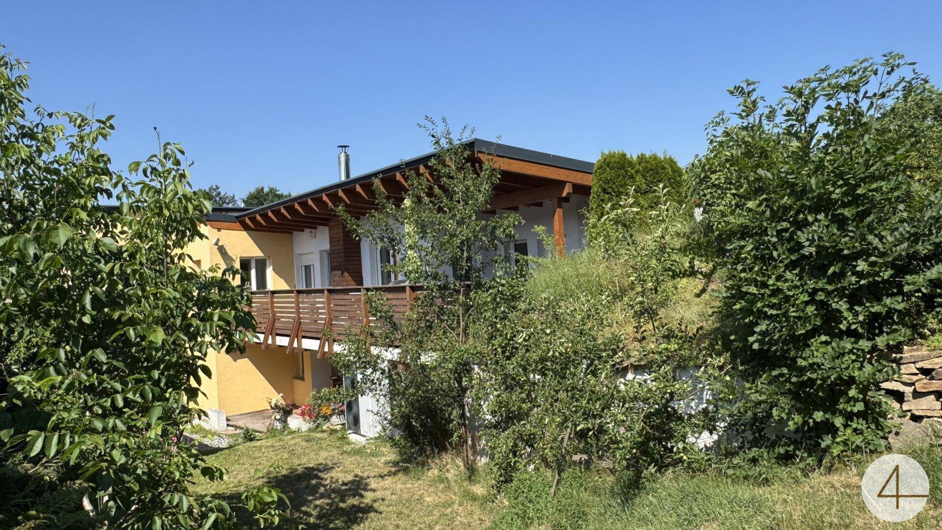 Wohnhaus mit gelber Fassade und Holzverkleidung, umgeben von üppigem Grün und Bäumen.