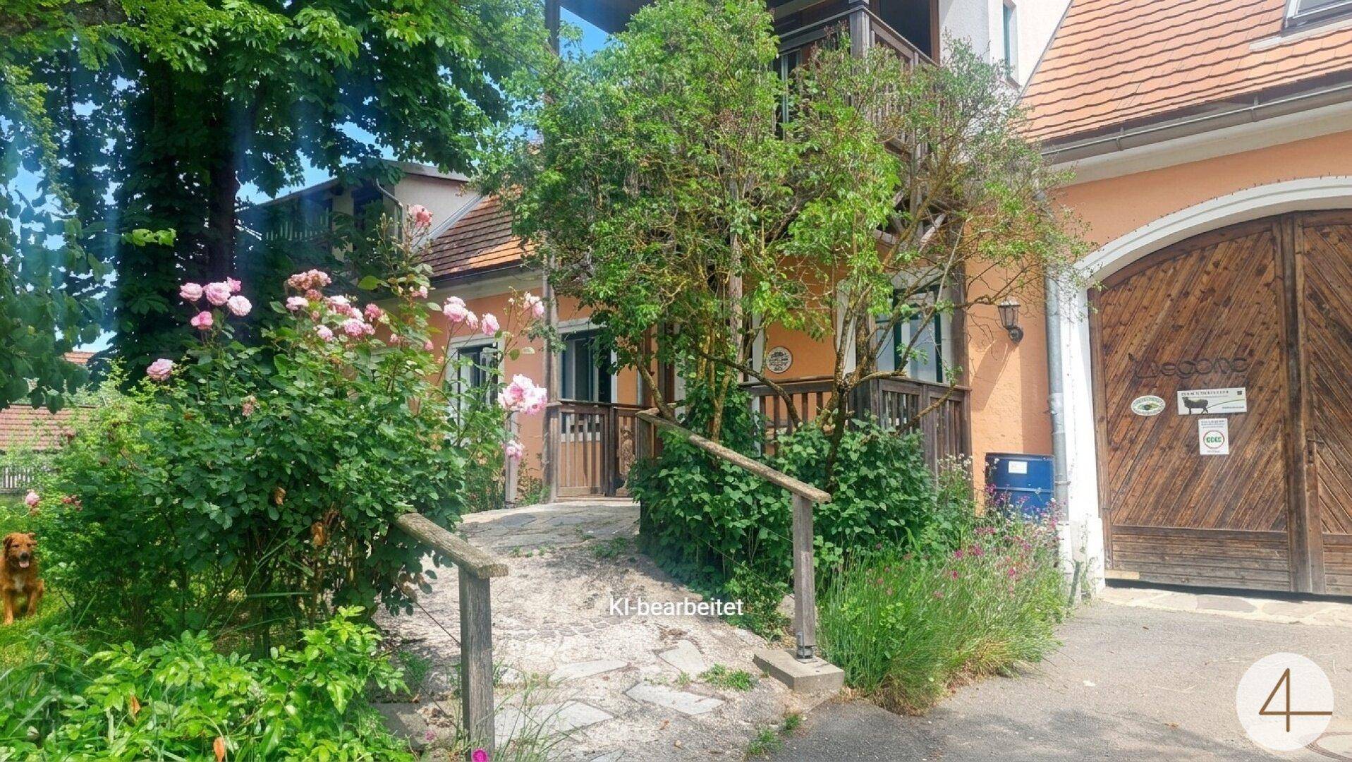 Eingangsbereich des Hauses mit einem Steinweg, Holzgeländer und blühenden Rosenbüschen im Vorgarten.