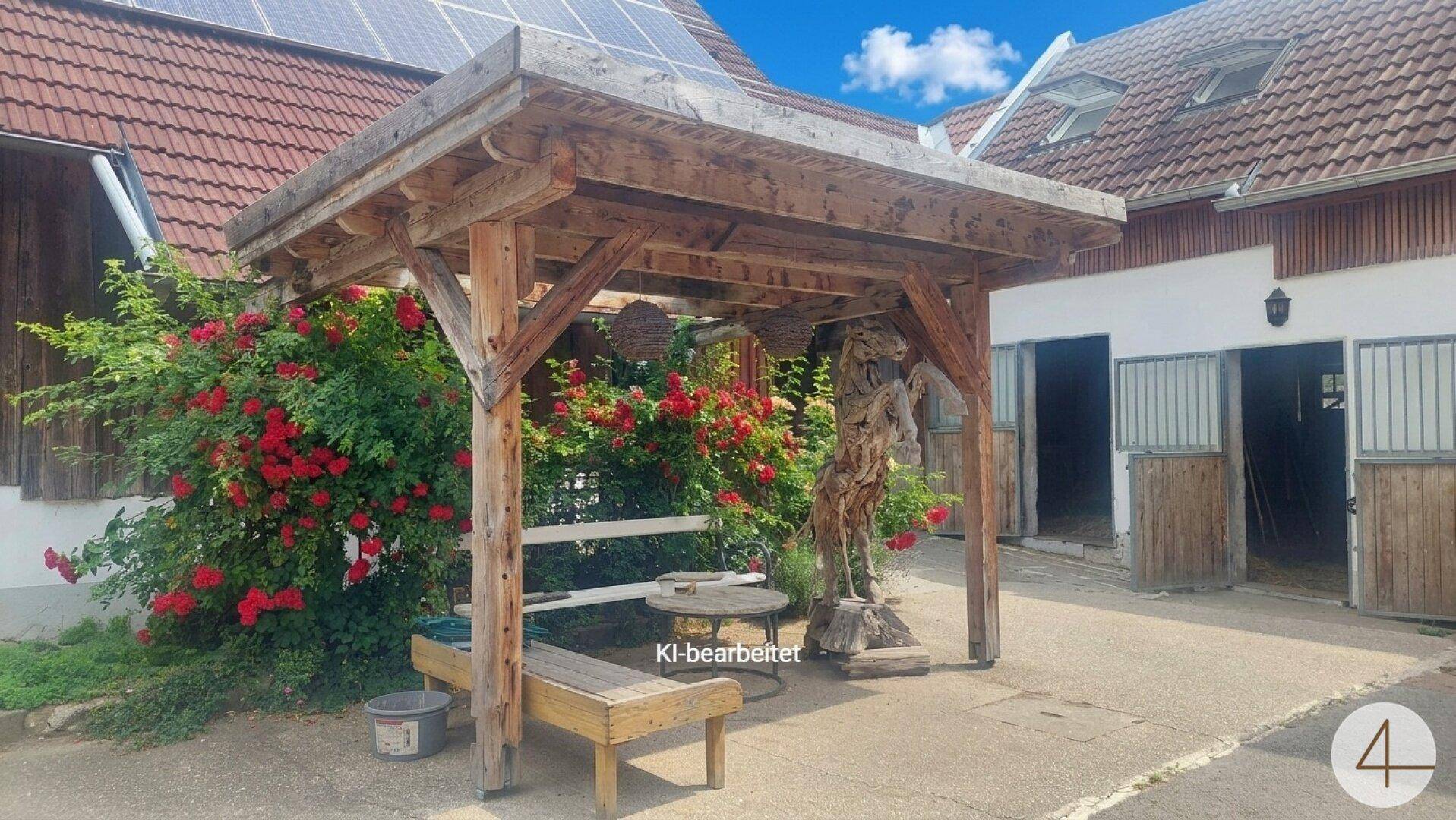 Rustikale Holzpergola mit Sitzgelegenheiten, umgeben von leuchtend roten Rosen und einem Gebäude mit Solaranlage.