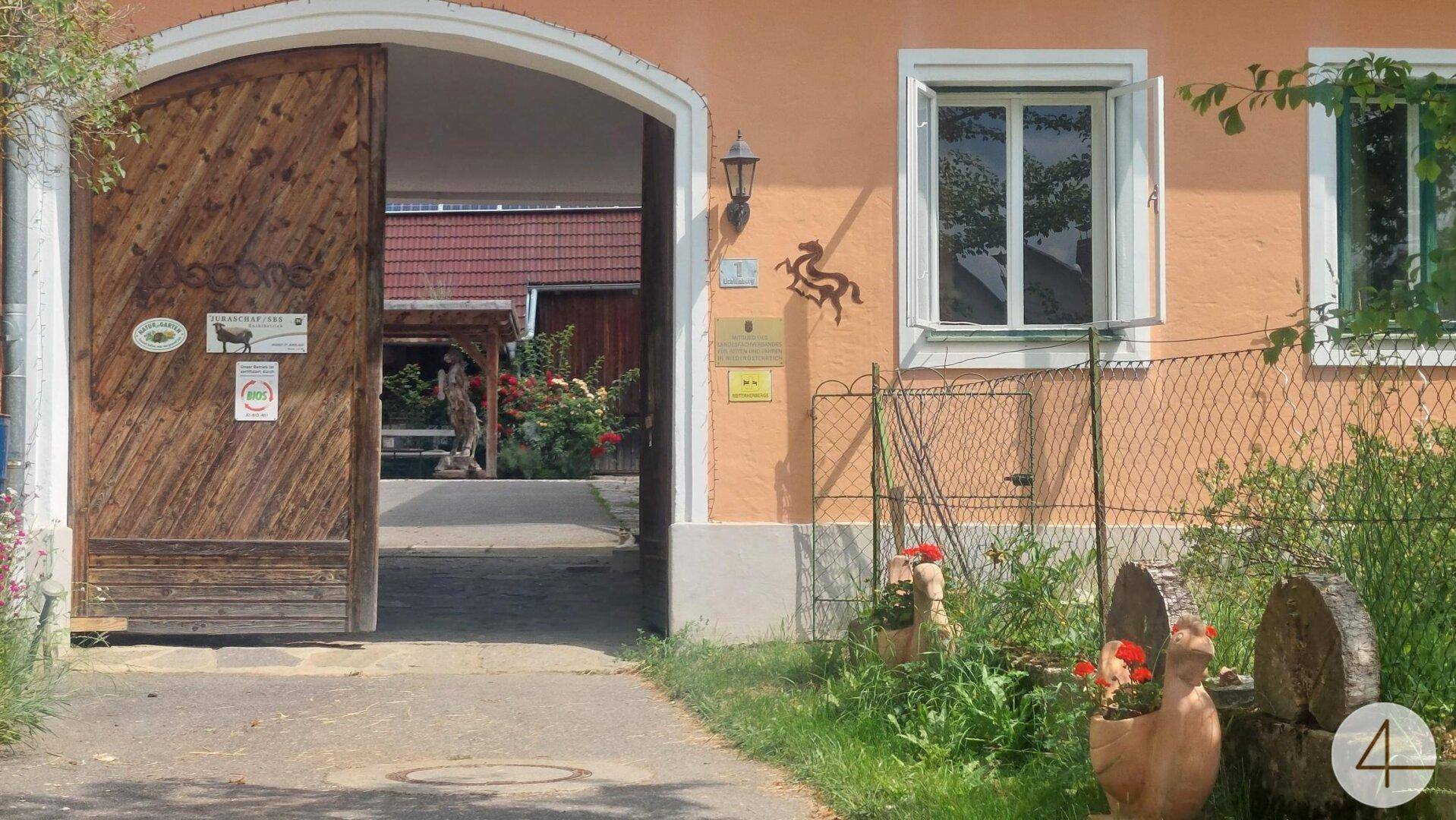 Detailansicht des großen Holztors und der Hausfassade mit Fenster und Gartenornamenten.