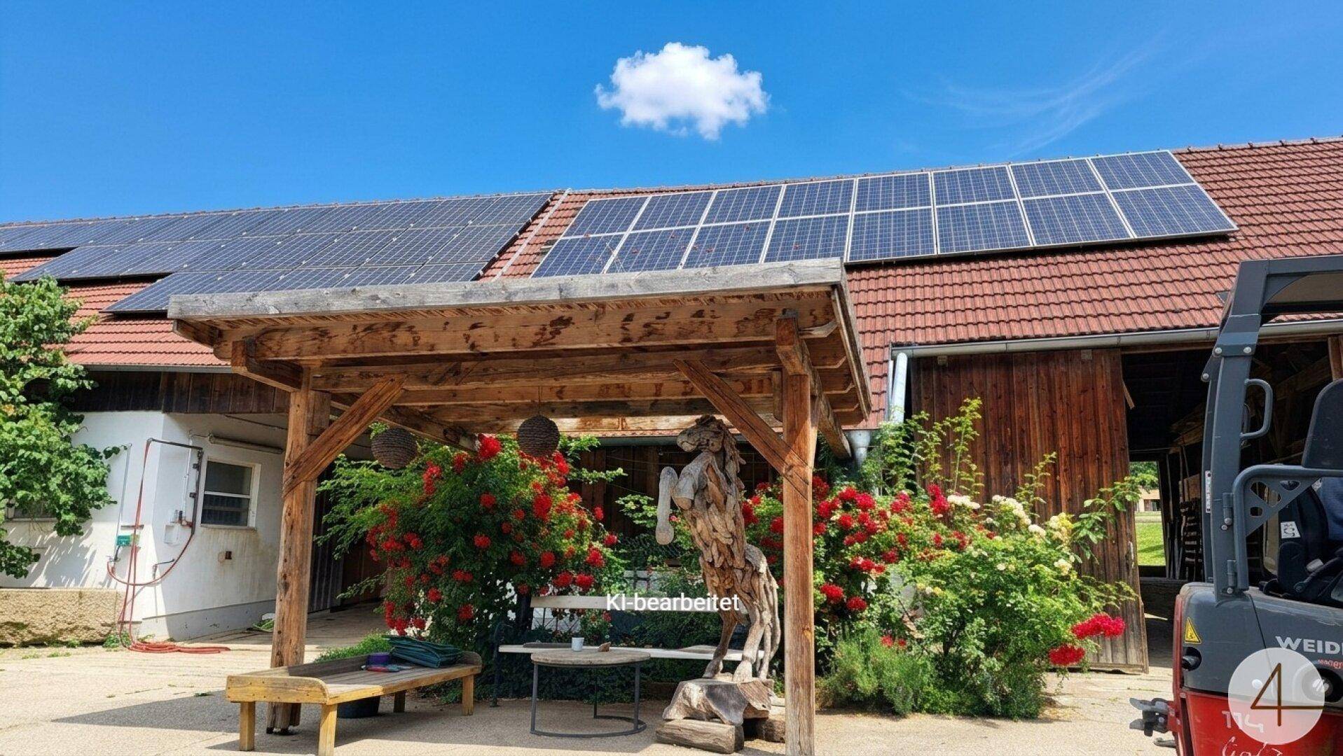 Gebäude mit Photovoltaikanlage auf dem Ziegeldach und einer Holzpergola mit Sitzgelegenheit und Rosen.